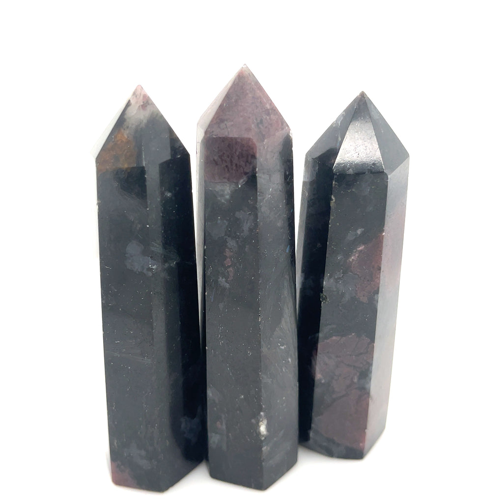 A group of  three dark colored gemstone towers arranged in a row, with a variation in size and shape, representing the Garnet and Astrophyllite gemstones on a white background overview. 