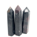 A group of  three dark colored gemstone towers arranged in a row, with a variation in size and shape, representing the Garnet and Astrophyllite gemstones on a white background overview. 
