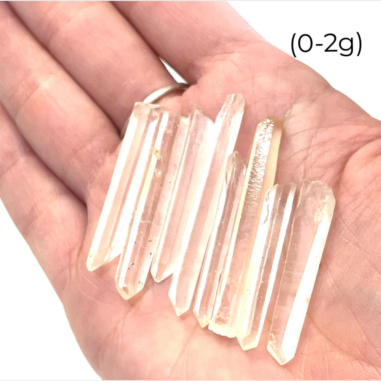 A hand holding a group of (0-2g) of clear quartz gemstone wands with a white background, front view.