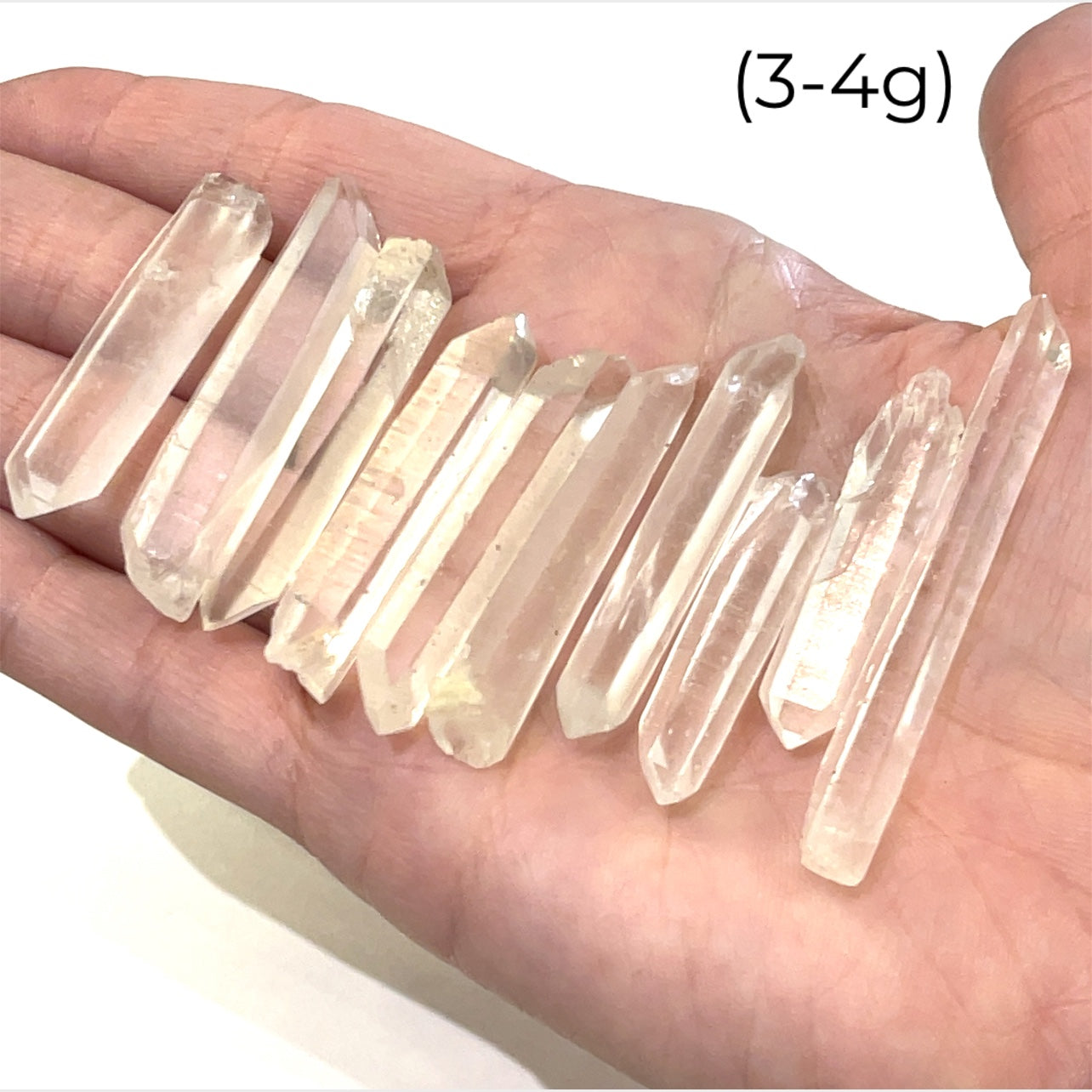 A hand holding a group of (3-4g) of clear quartz gemstone wands with a white background, front view.
