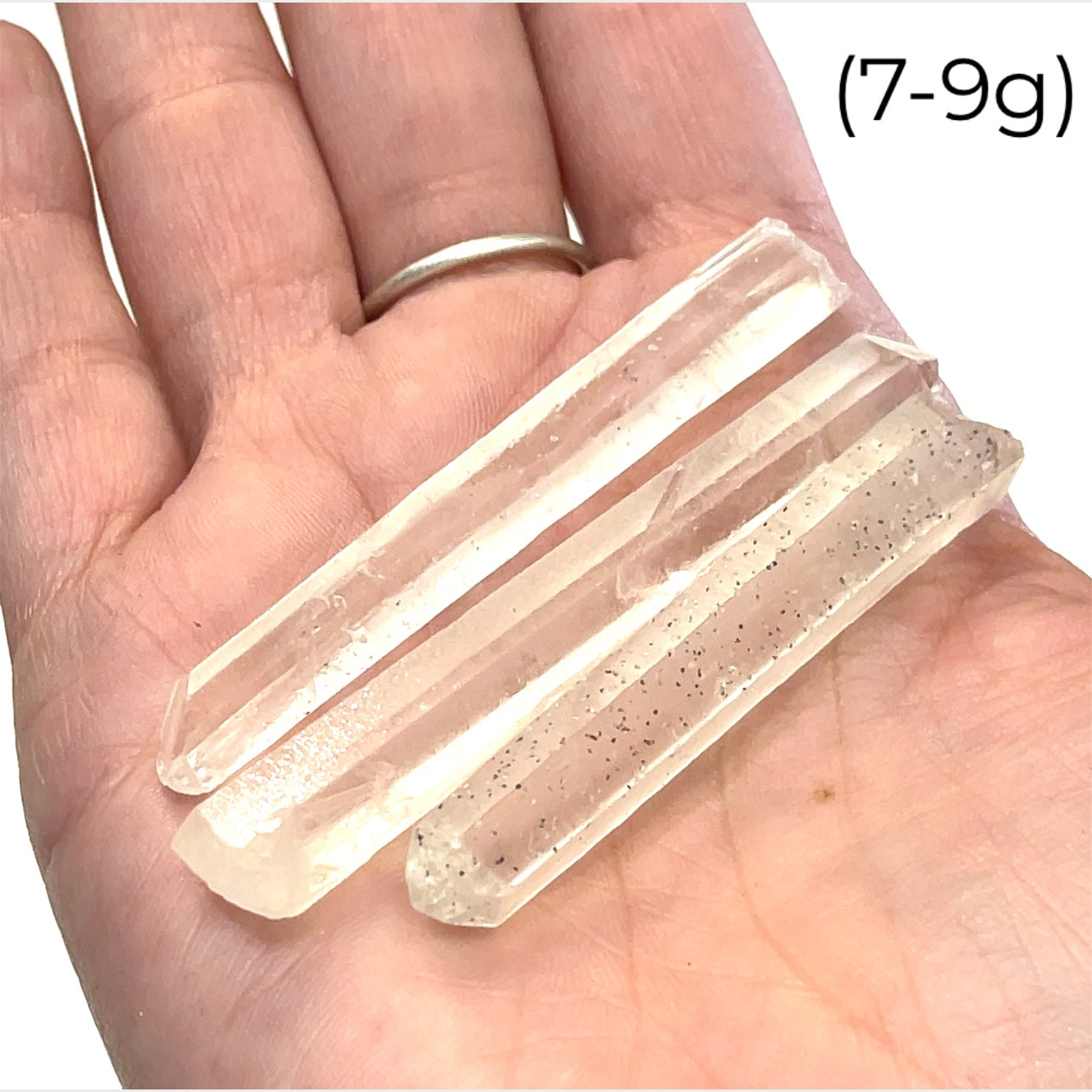 A hand holding a group of (7-9g) of clear quartz gemstone wands with a white background, front view.
