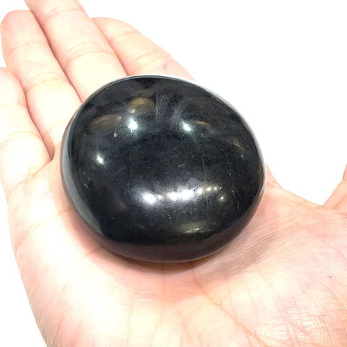 A hand holding a polished Black Tourmaline gemstone palm stone on a white background, front view. 