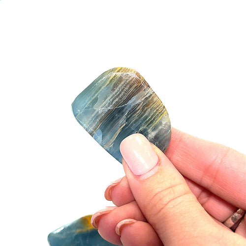 A hand holding a polished Blue Onyx gemstone with a striped pattern on a white background, front view. 