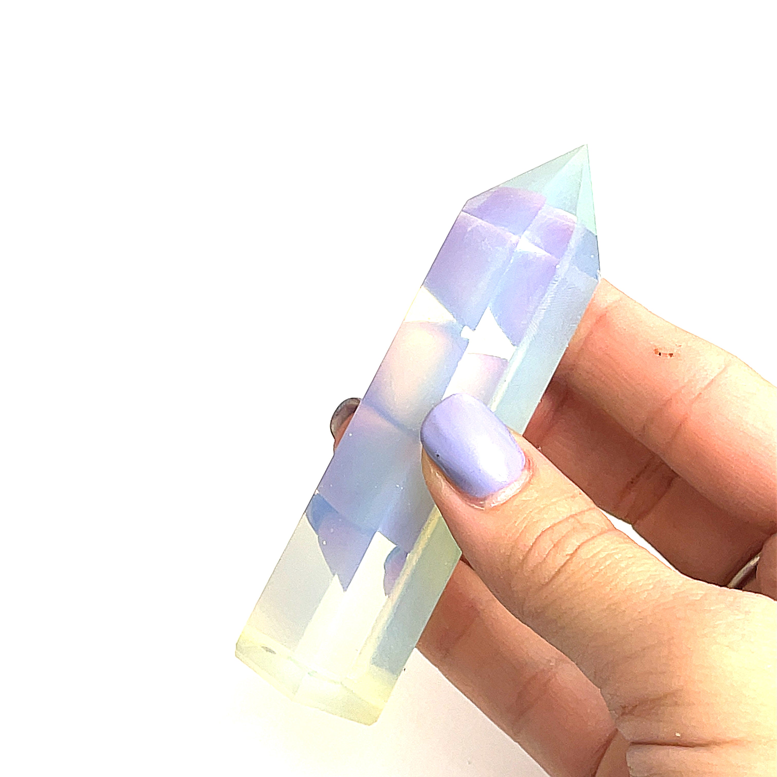 A hand holding a transparent multicolored opalite gemstone tower against a white background, front view. 