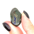 A hand holding a tumbled Azurite gemstone with visible Malachite inclusions on a white background, front view.