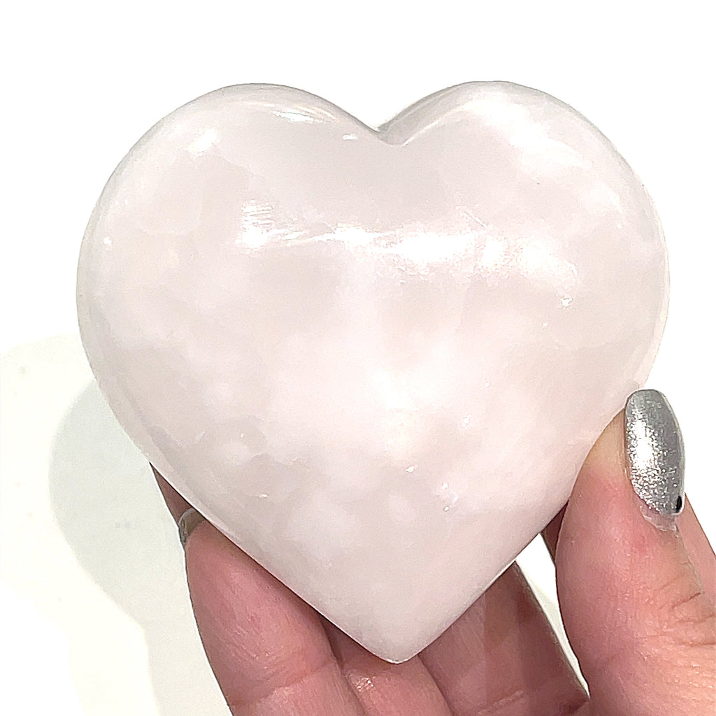 A hand holding an XL pink Mangano Calcite gemstone heart on a white background, front view.