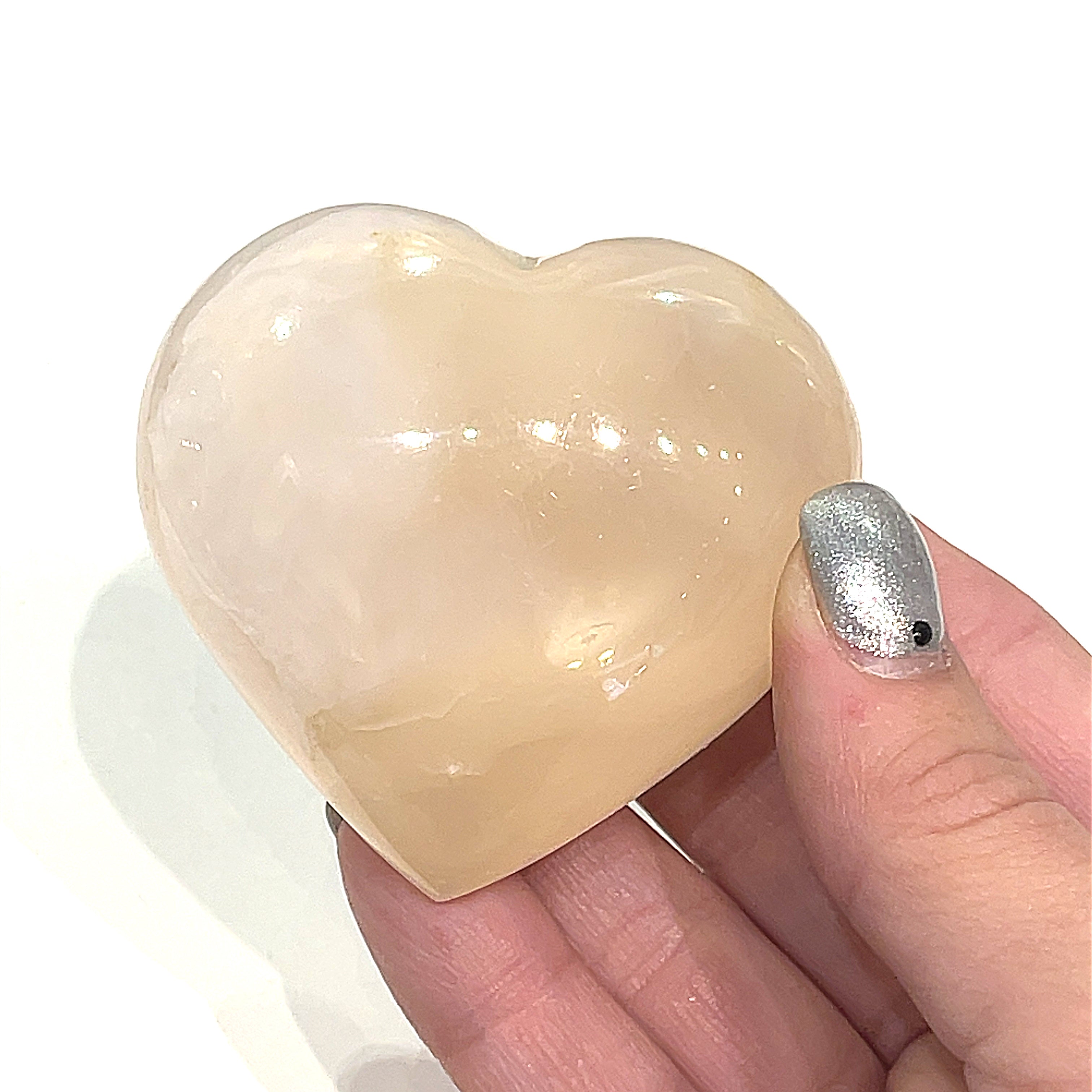 A hand holding one pink Mangano Calcite gemstone heart on a white background, front view.