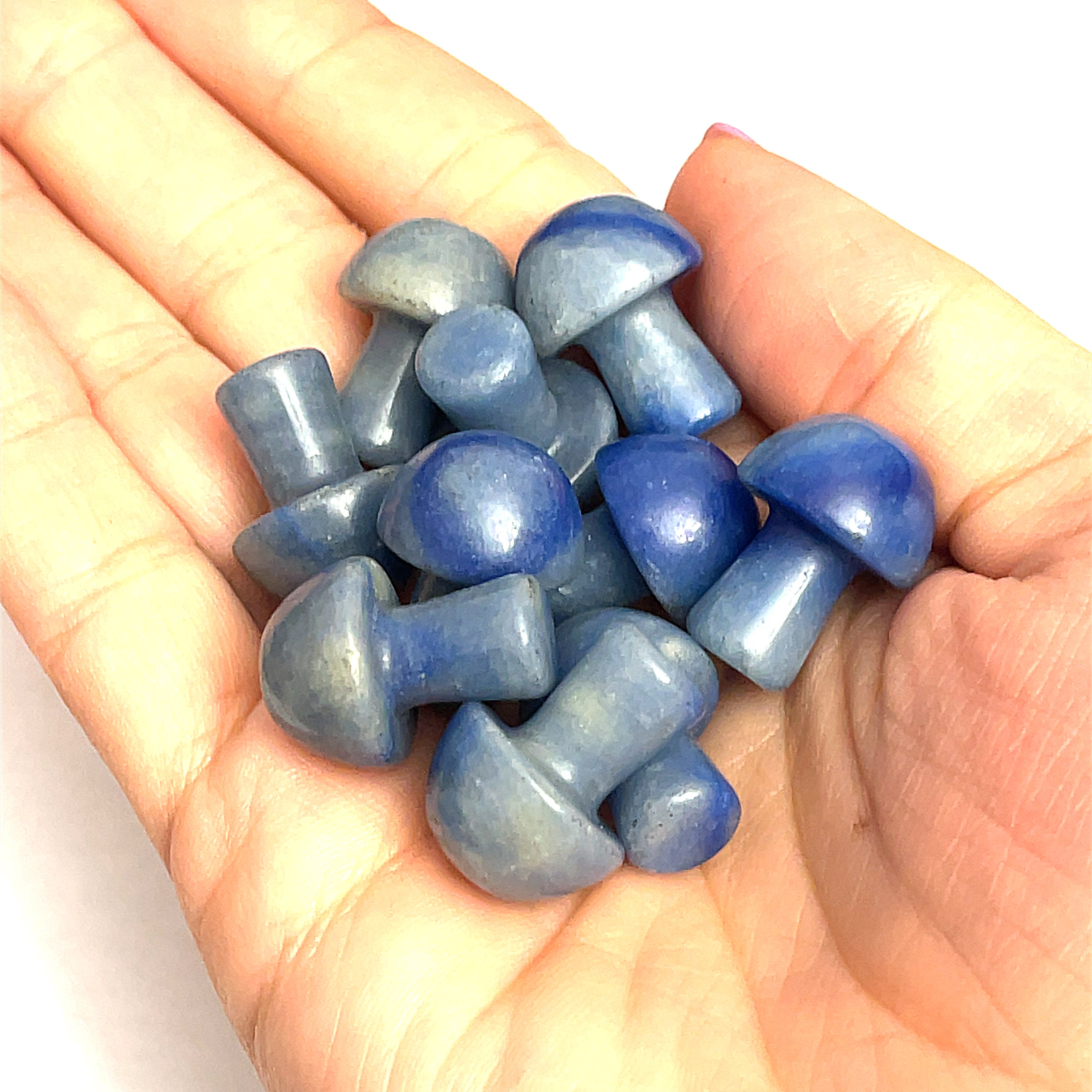 A hand holding several Blue Aventurine mini mushroom-shaped gemstone carvings on a white background, front view. 