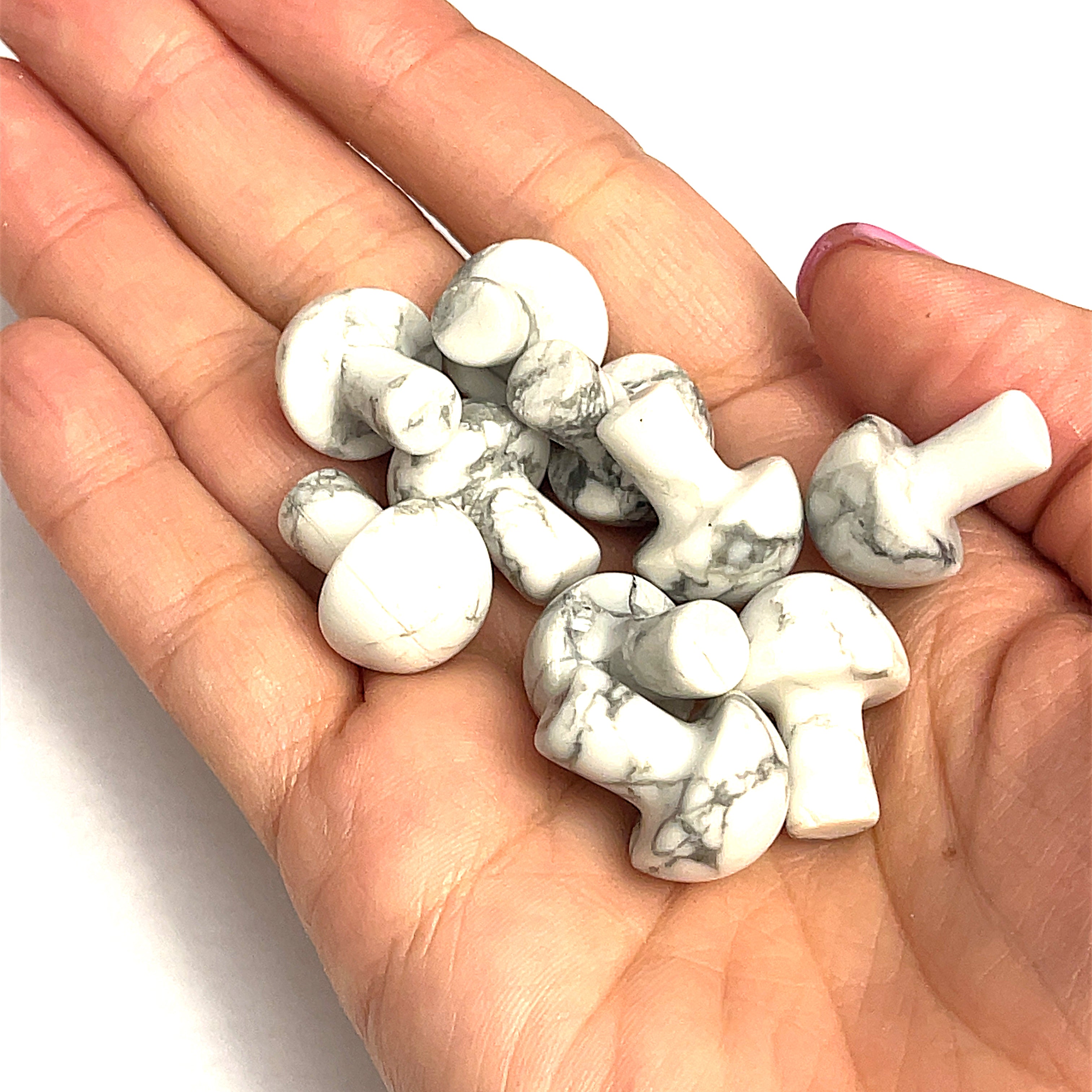 A hand holding several Howlite mini mushroom-shaped gemstone carvings on a white background, front view. 