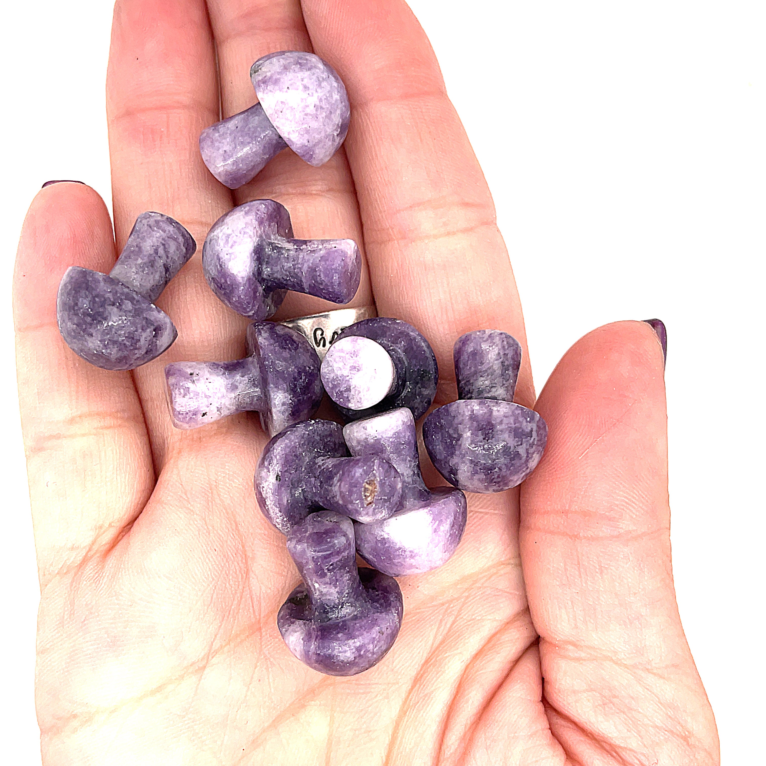 A hand holding several Lepidolite mini mushroom-shaped gemstone carvingson a white background, front view. 