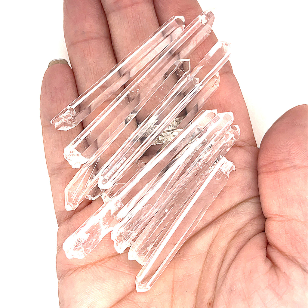 A hand holding several clear quartz gemstone wands with a white background, front view.