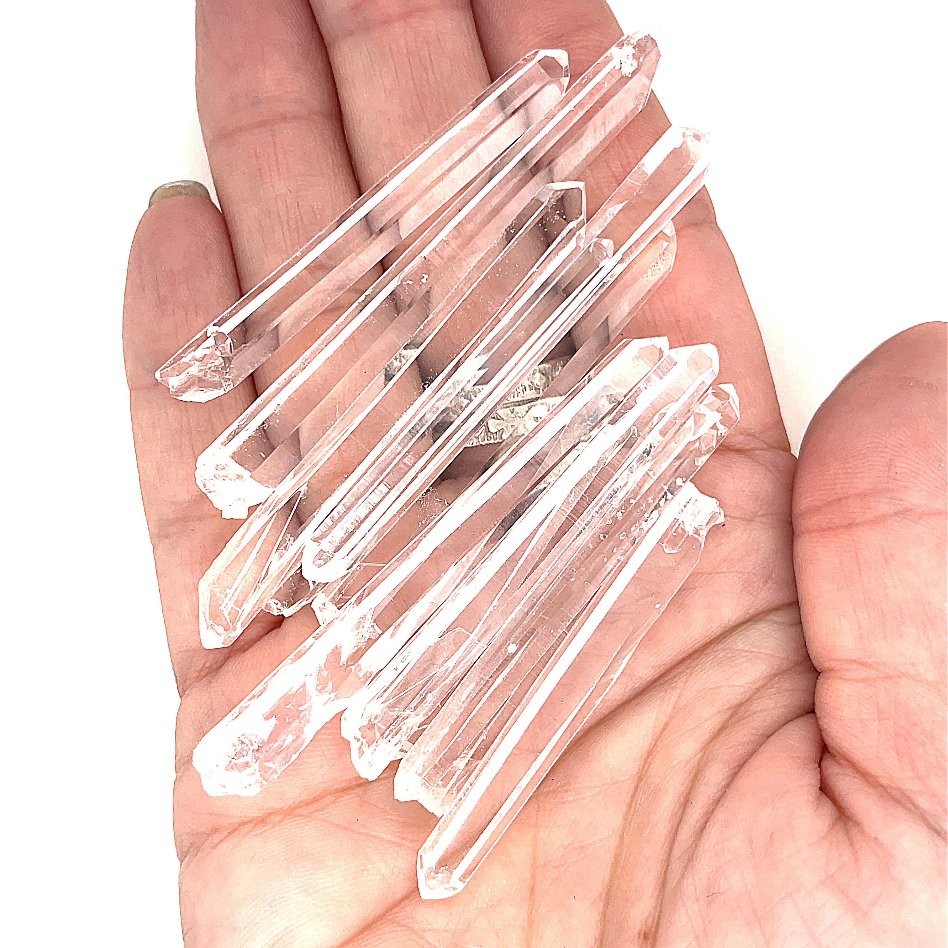 A hand holding several clear quartz gemstone wands with a white background, front view.