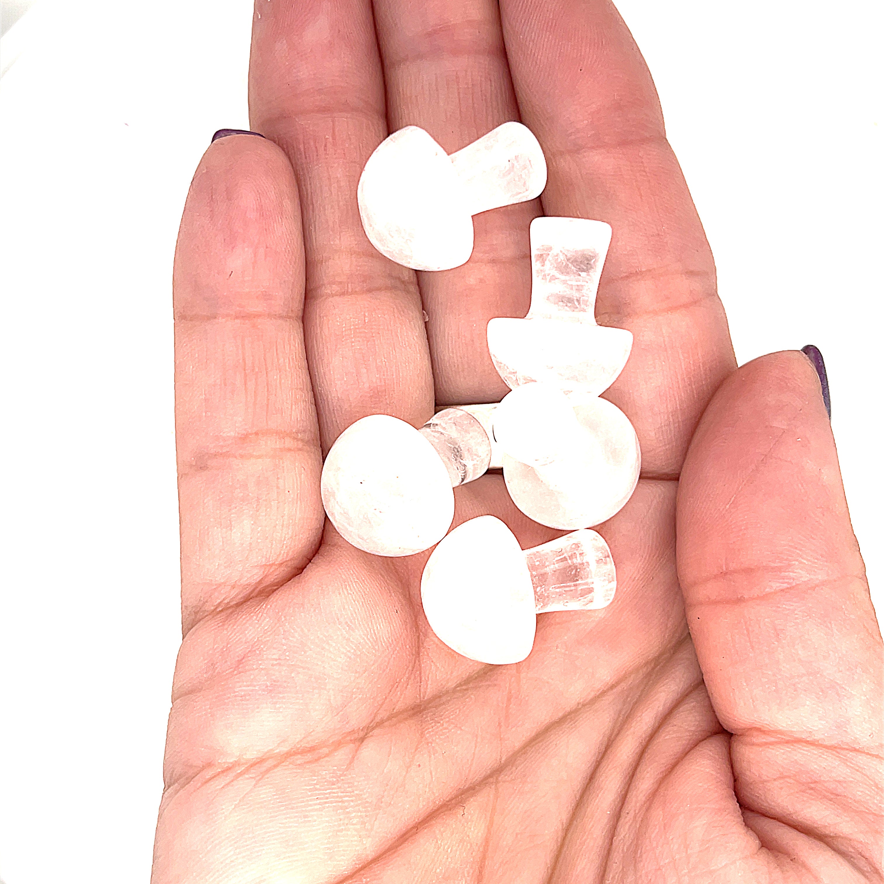 A hand holding several clear quartz  mini mushroom-shaped gemstone carvingson a white background, front view. 