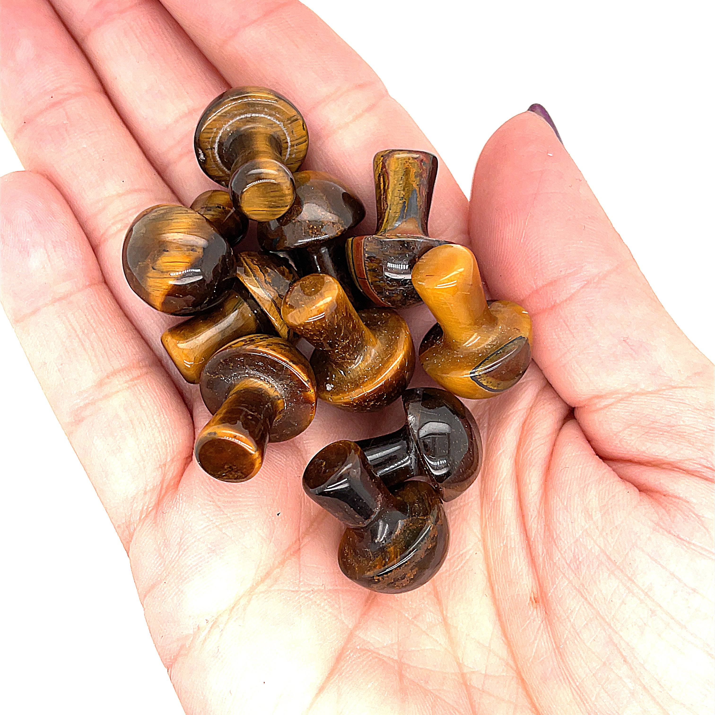A hand holding several golden tiger eye mini mushroom-shaped gemstone carvings on a white background, front view. 