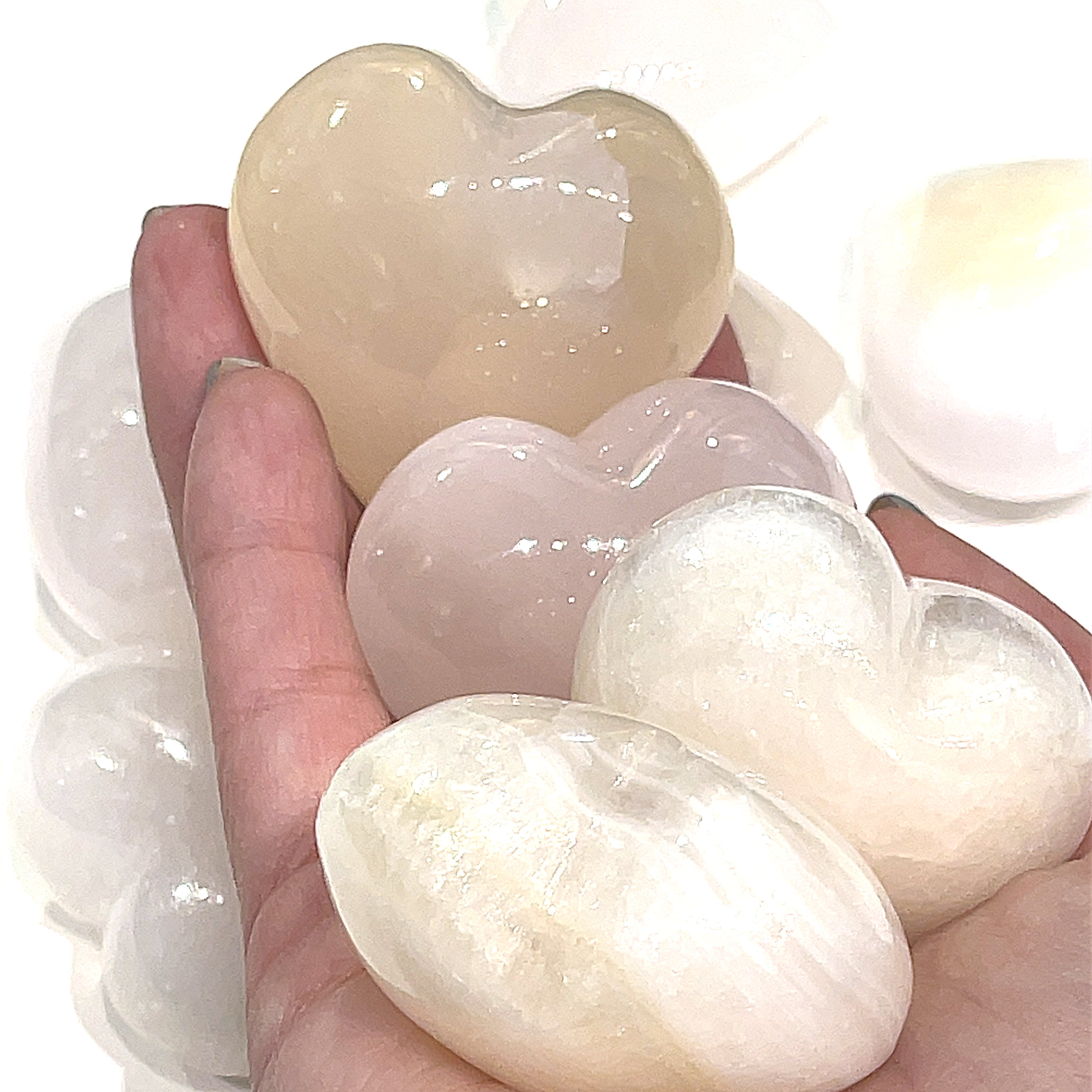 A hand holding several pink Mangano Calcite gemstone heart on a white background, front view.