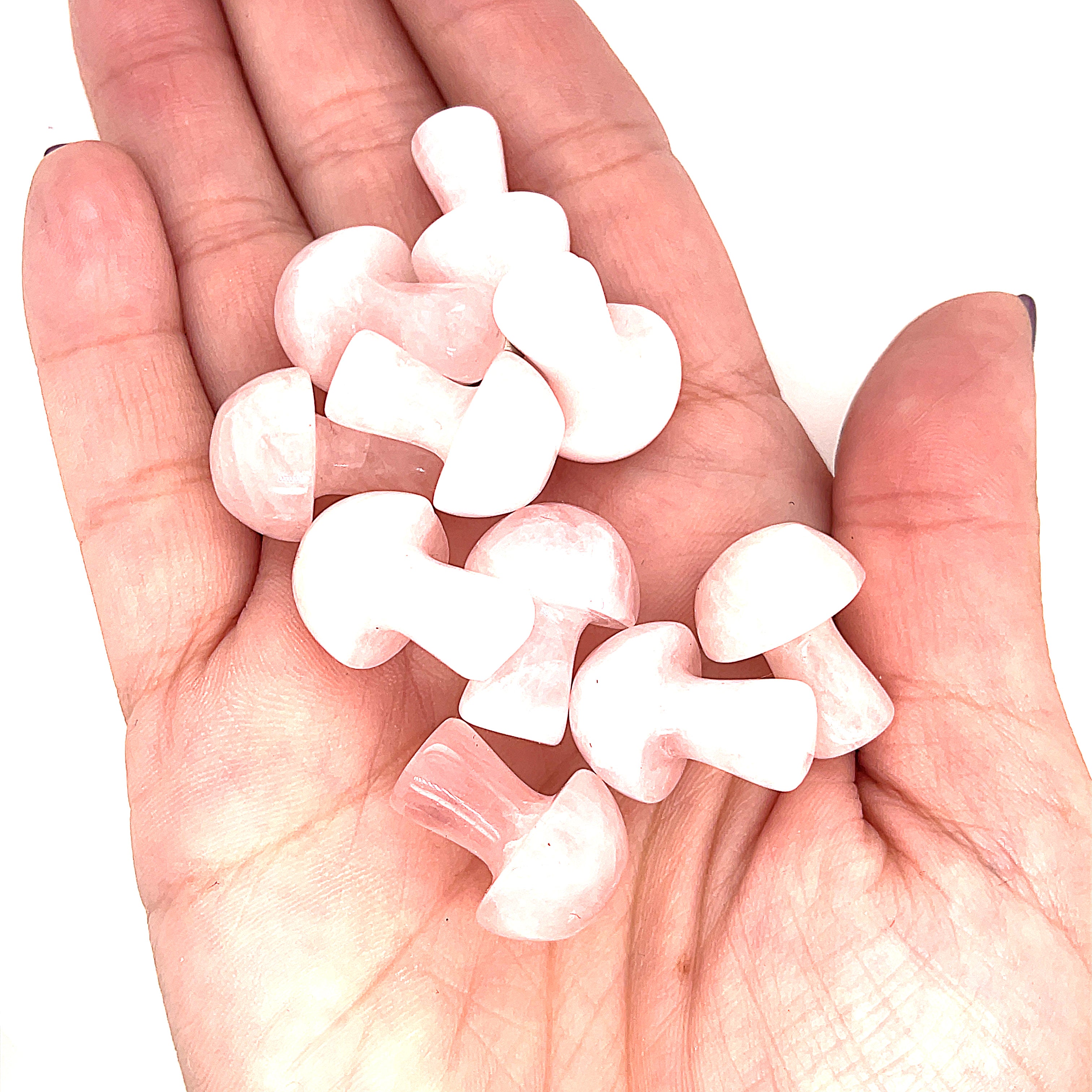 A hand holding several rose quartz  mini mushroom-shaped gemstone carvingson a white background, front view. 