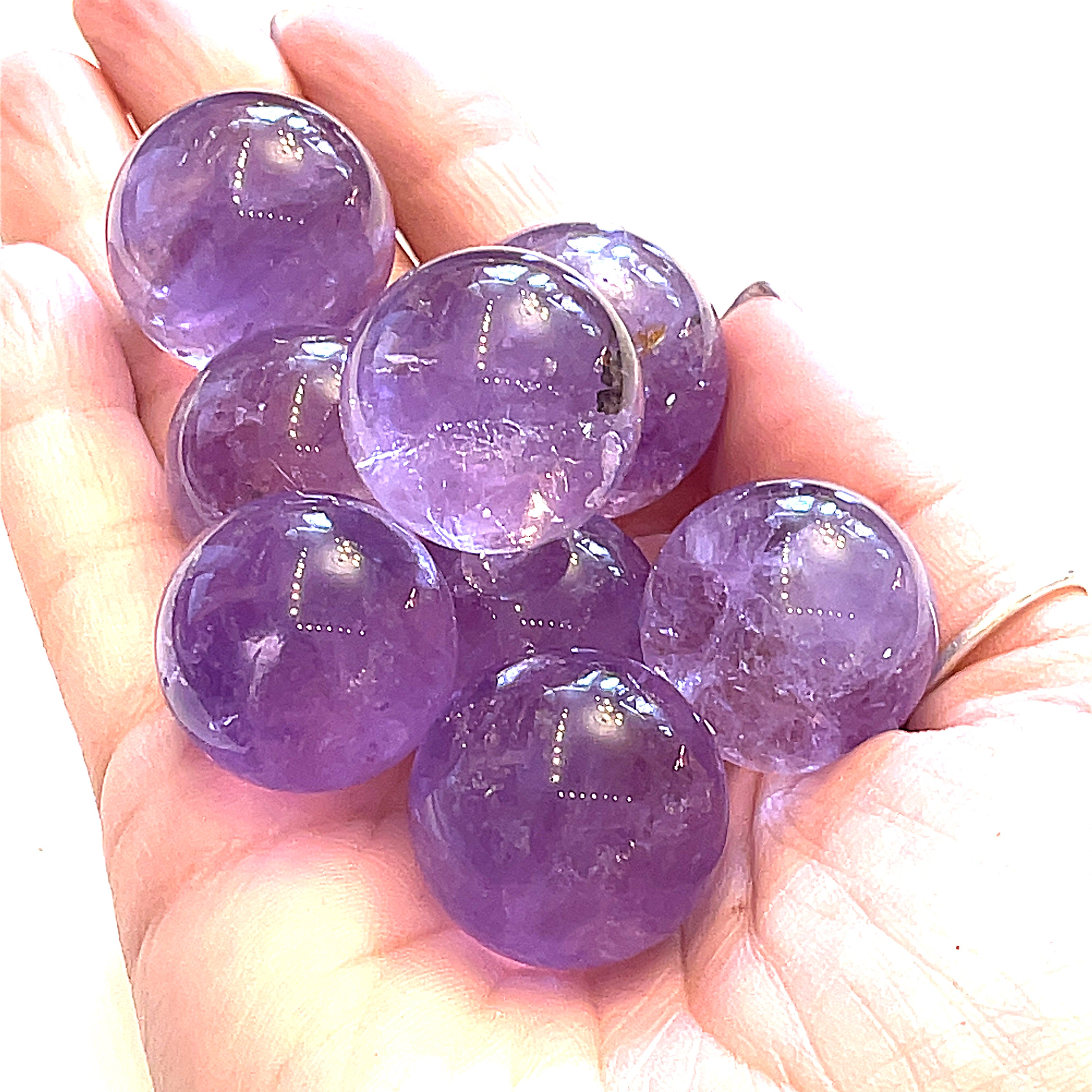 A hand holding several small purple amethyst gemstone spheres on a white background, front close-up overview. 