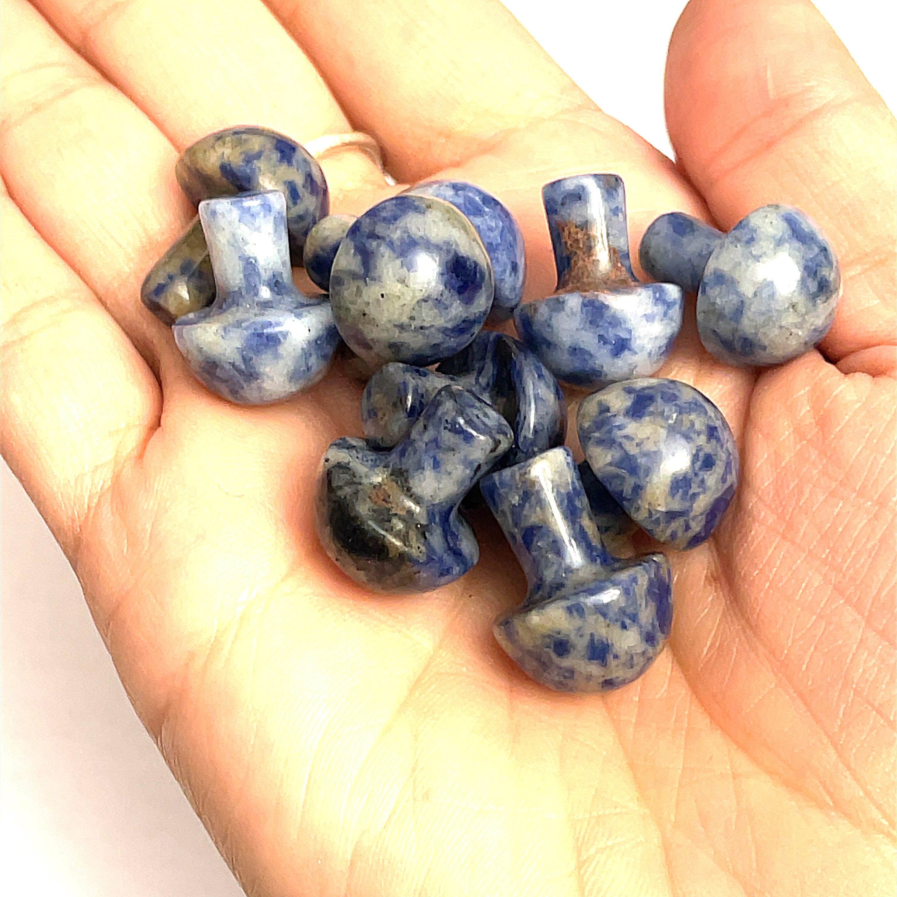 A hand holding several sodalite mini mushroom-shaped gemstone carvings on a white background, front view. 