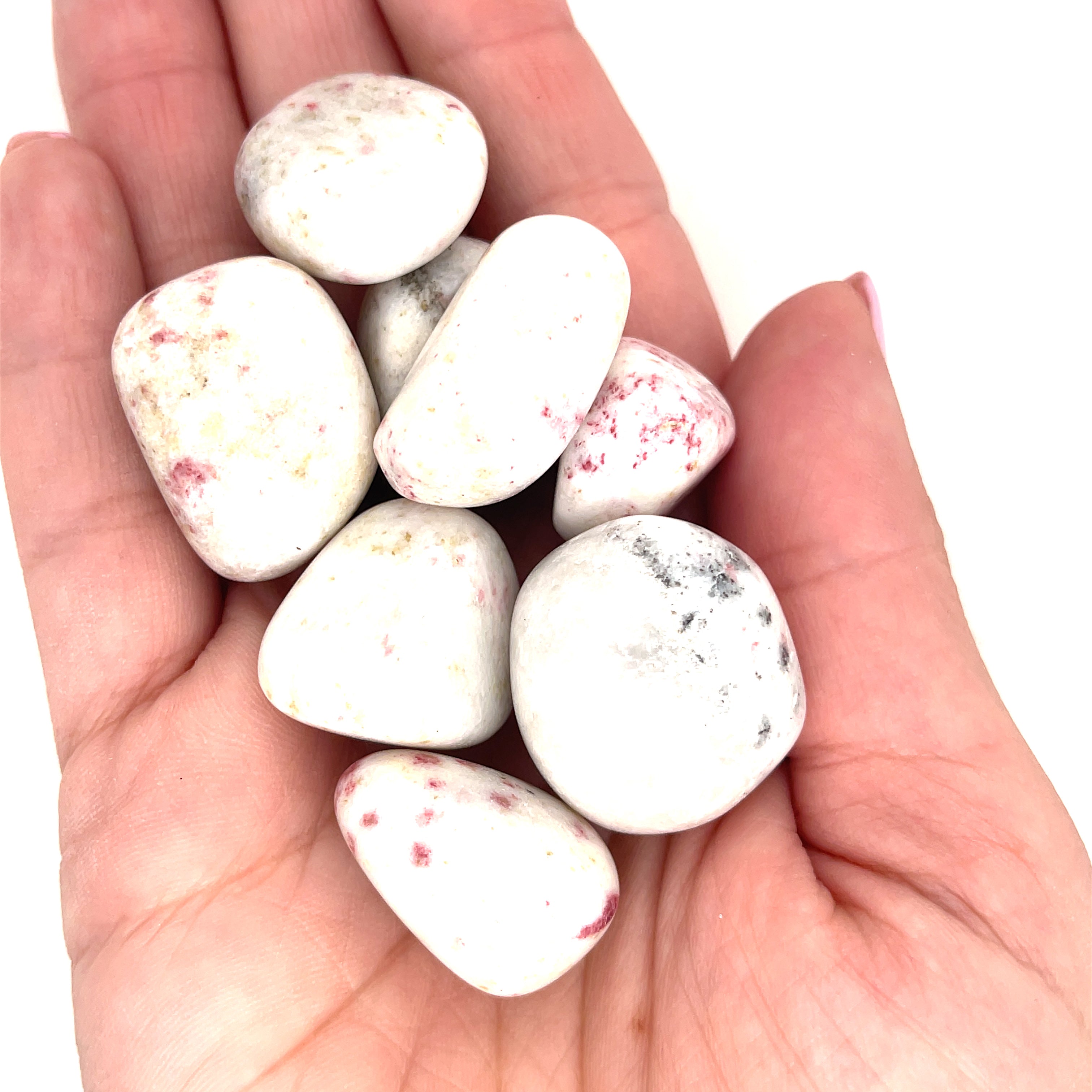 A hand holding several tumbled Cinnabar gemstones with a white and red speckled appearance on a white background, front, close-up view. 