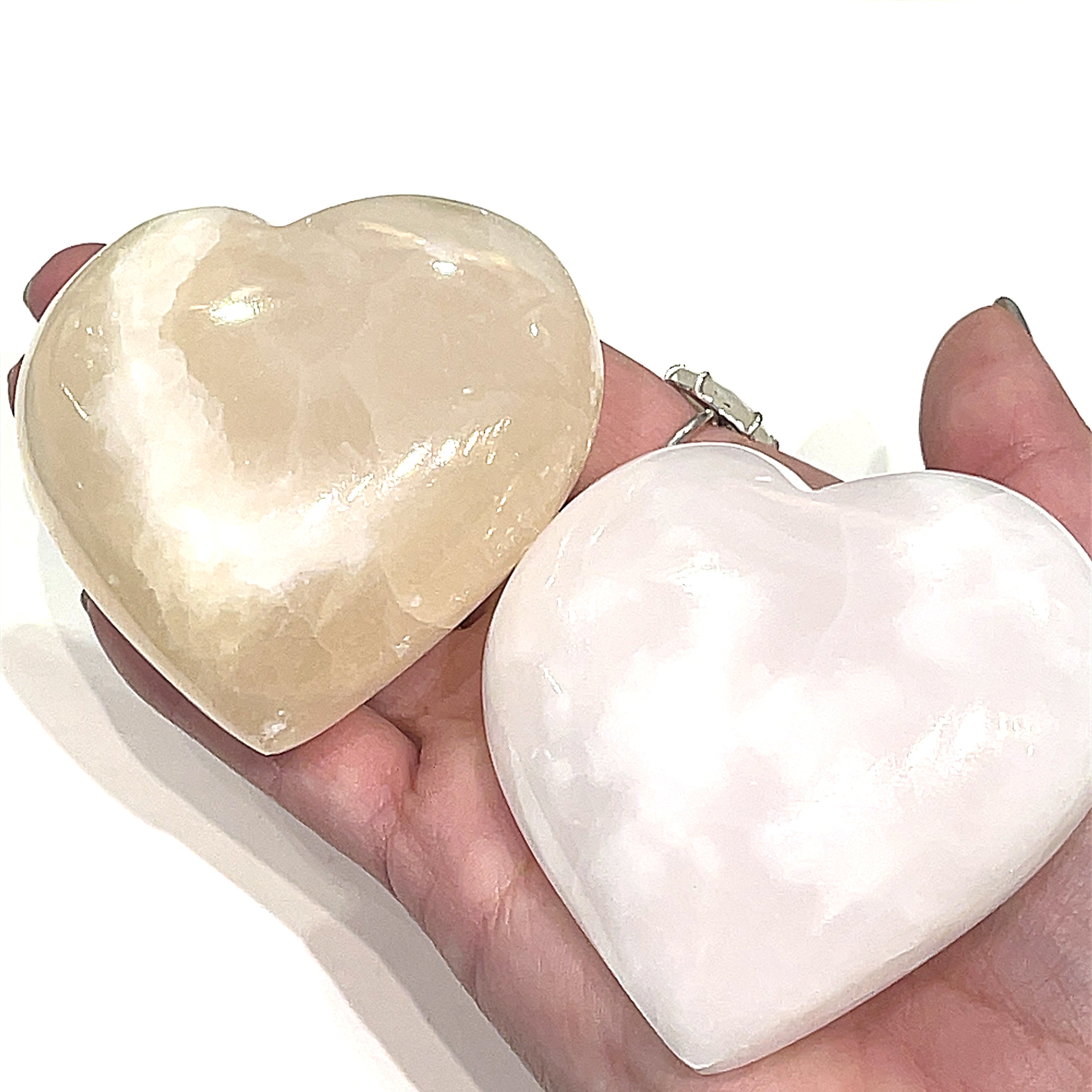 A hand holding two pink Mangano Calcite gemstone heart on a white background, front view.