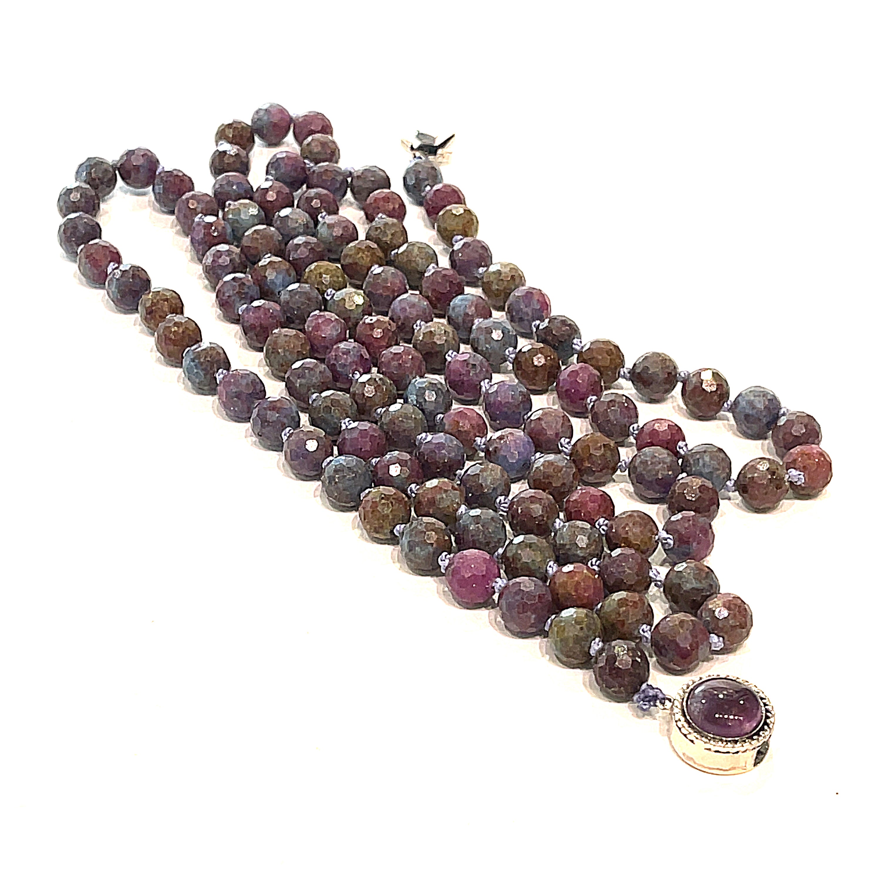 A knotted Ruby Kyanite gemstone necklace with a sterling silver amethyst box clasp, beads are 6mm faceted round, long center, close-up, overview on a white background.