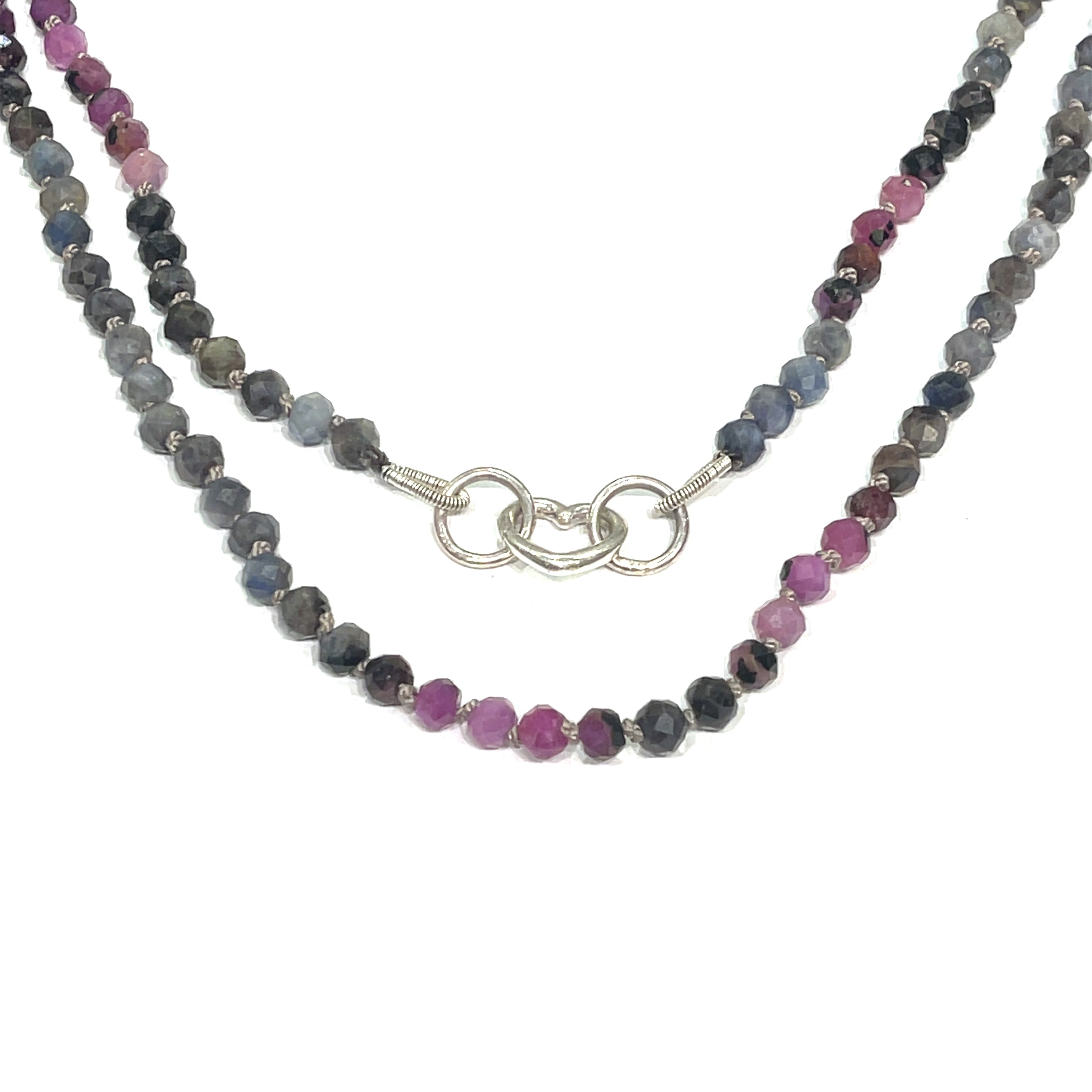 A knotted necklace featuring a heart lobster clasp, composed of faceted roundel rubies and sapphire gemstones on a white background, hanging in the center close up overview. 