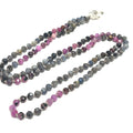 A knotted necklace featuring a heart lobster clasp, composed of faceted roundel rubies and sapphire gemstones on a white background, long center view. 