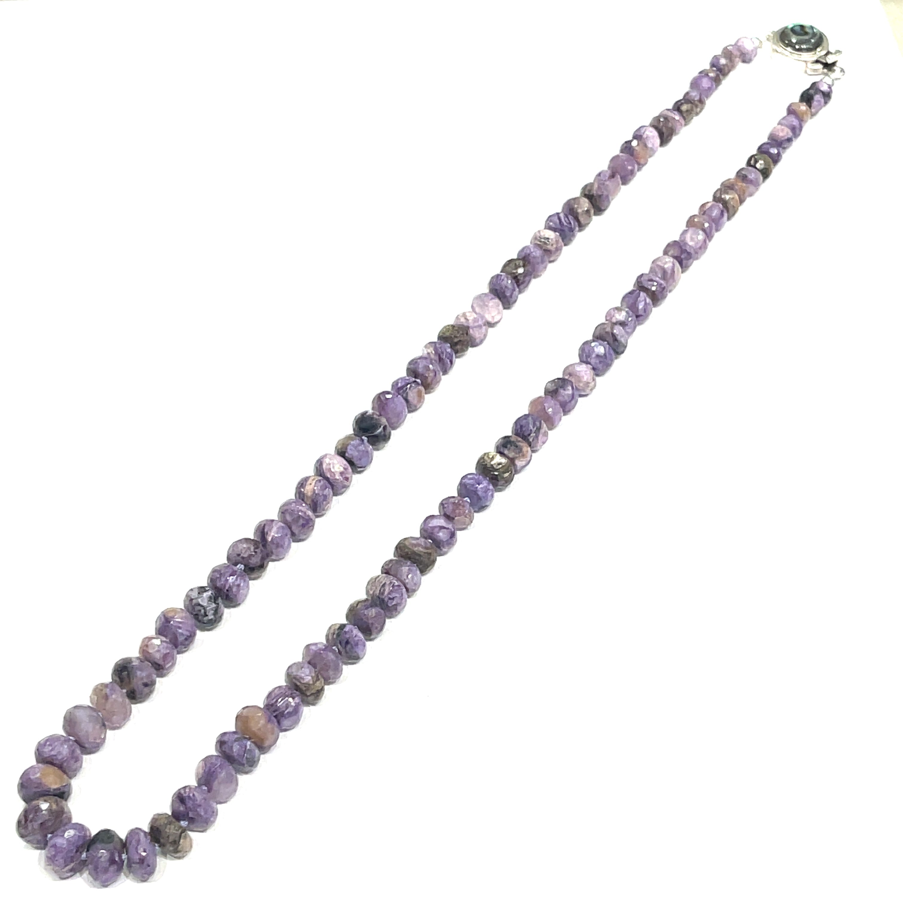 A knotted necklace featuring a heart lobster clasp, composed of faceted roundel rubies and sapphire gemstones on a white background, long diagonal center close up overview. 