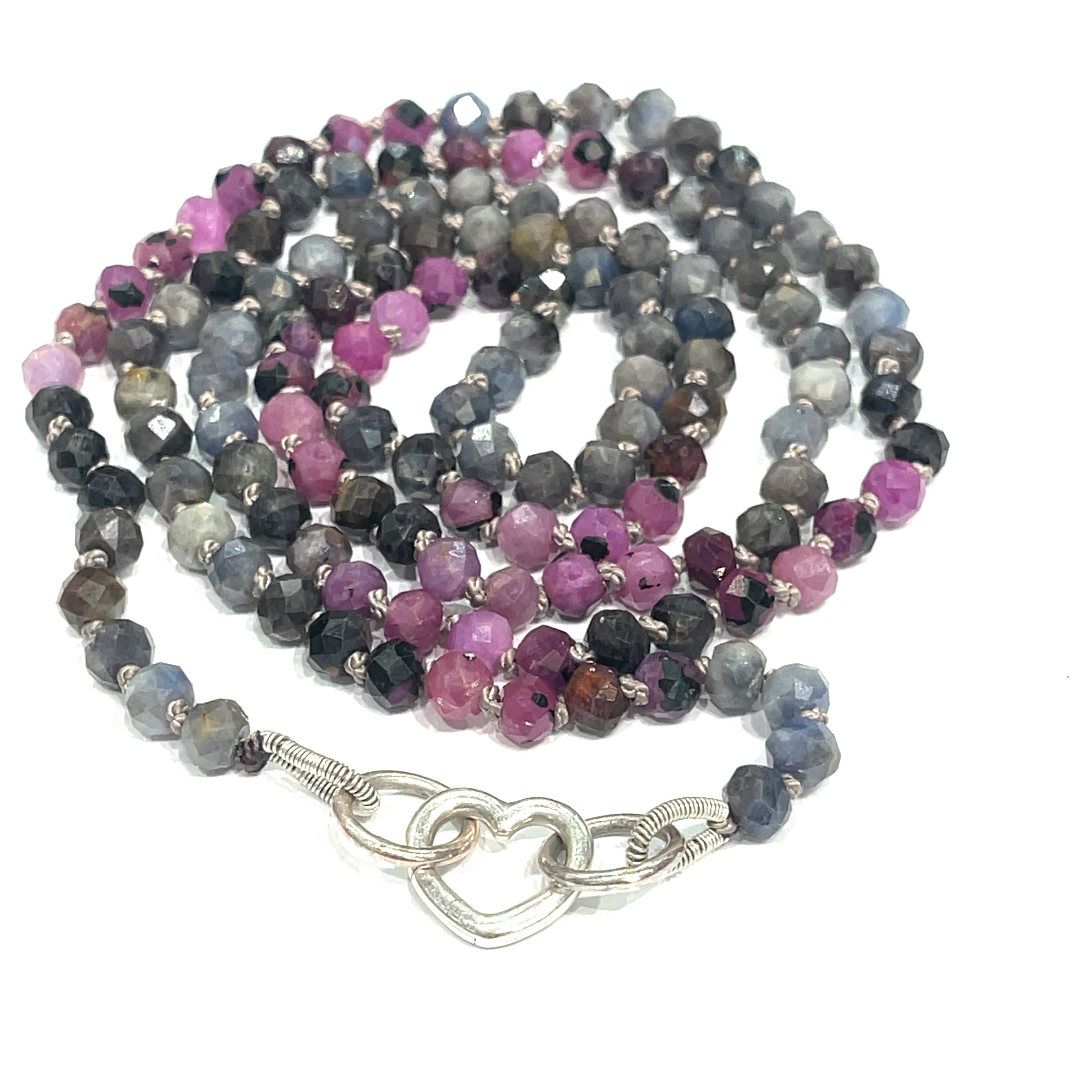 A knotted necklace featuring a heart lobster clasp, composed of faceted roundel rubies and sapphire gemstones on a white background, spiral center close up overview. 
