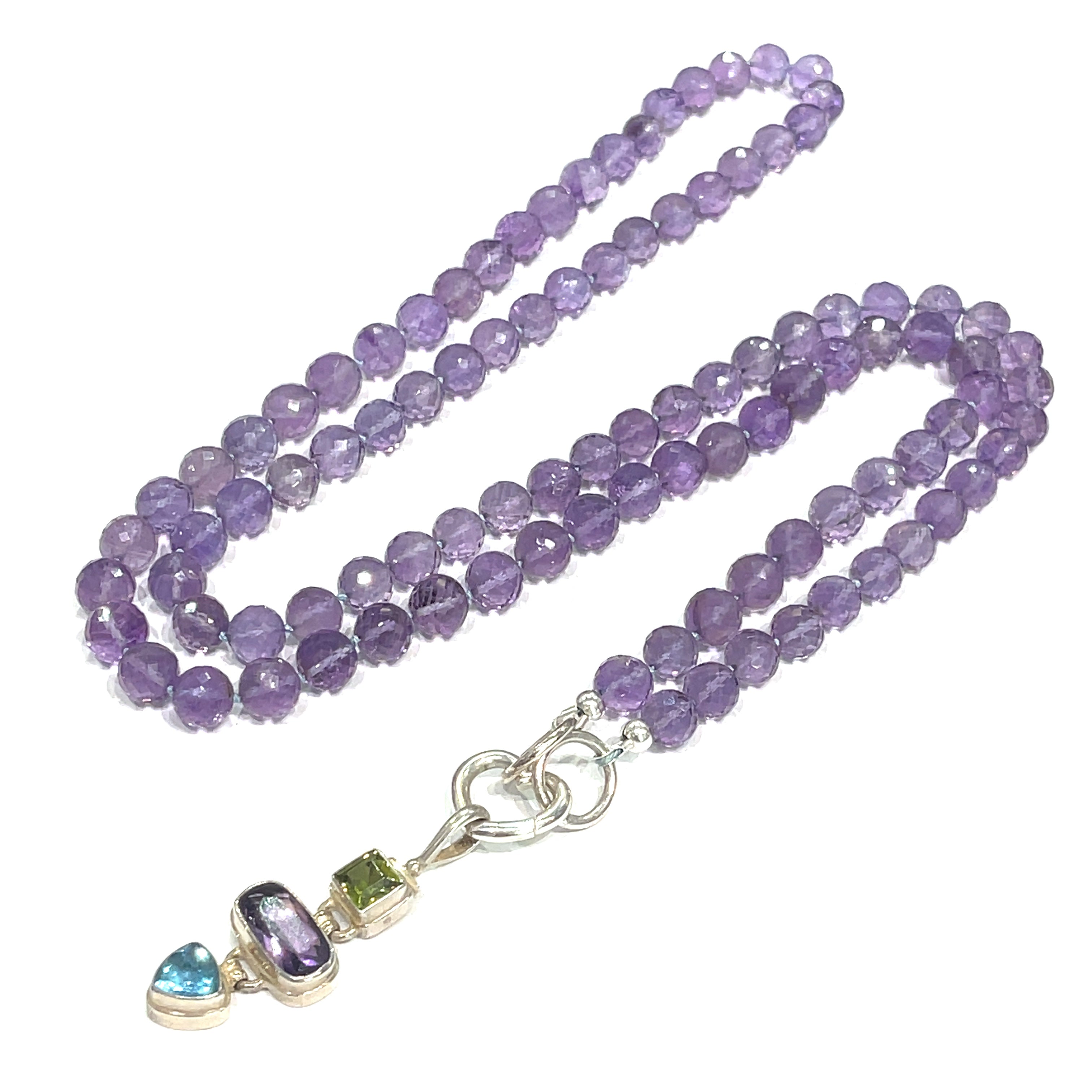 A knotted necklace featuring round Amethyst gemstones, a sterling silver heart clasp, and a silver gemstone pendant with Peridot and Blue Topaz, on a white background, long center front overview. 