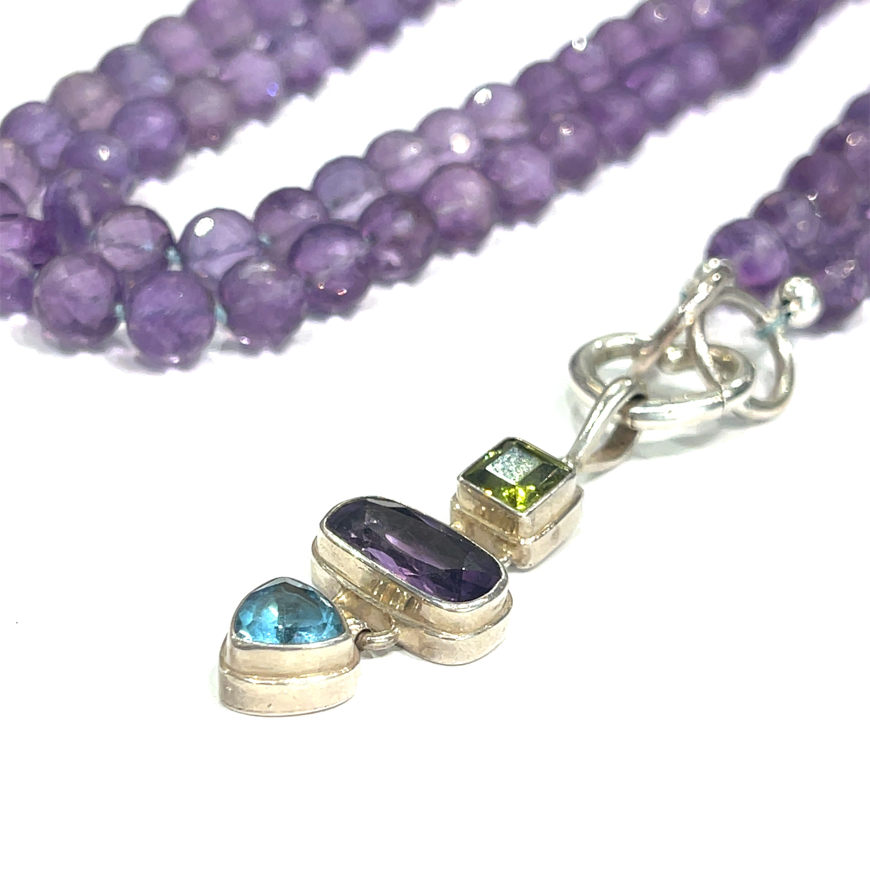 A knotted necklace featuring round Amethyst gemstones, a sterling silver heart clasp, and a silver gemstone pendant with Peridot and Blue Topaz, on a white background, pendant center front overview. 