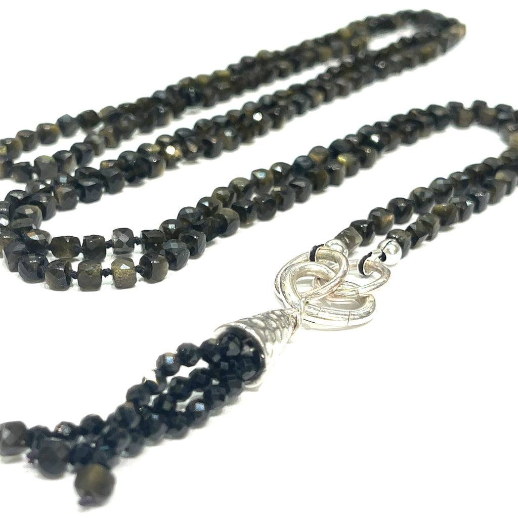 A knotted necklace made of Golden Sheen Obsidian gemstones with a tassel, featuring silver accents. On a white background, a long, center close up overview. 