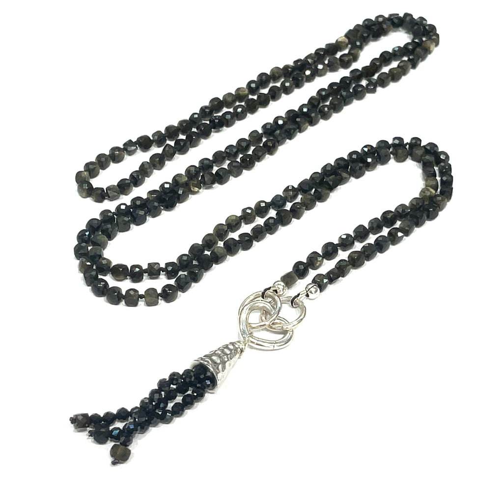 A knotted necklace made of Golden Sheen Obsidian gemstones with a tassel, featuring silver accents. On a white background, a long, center view overview. 