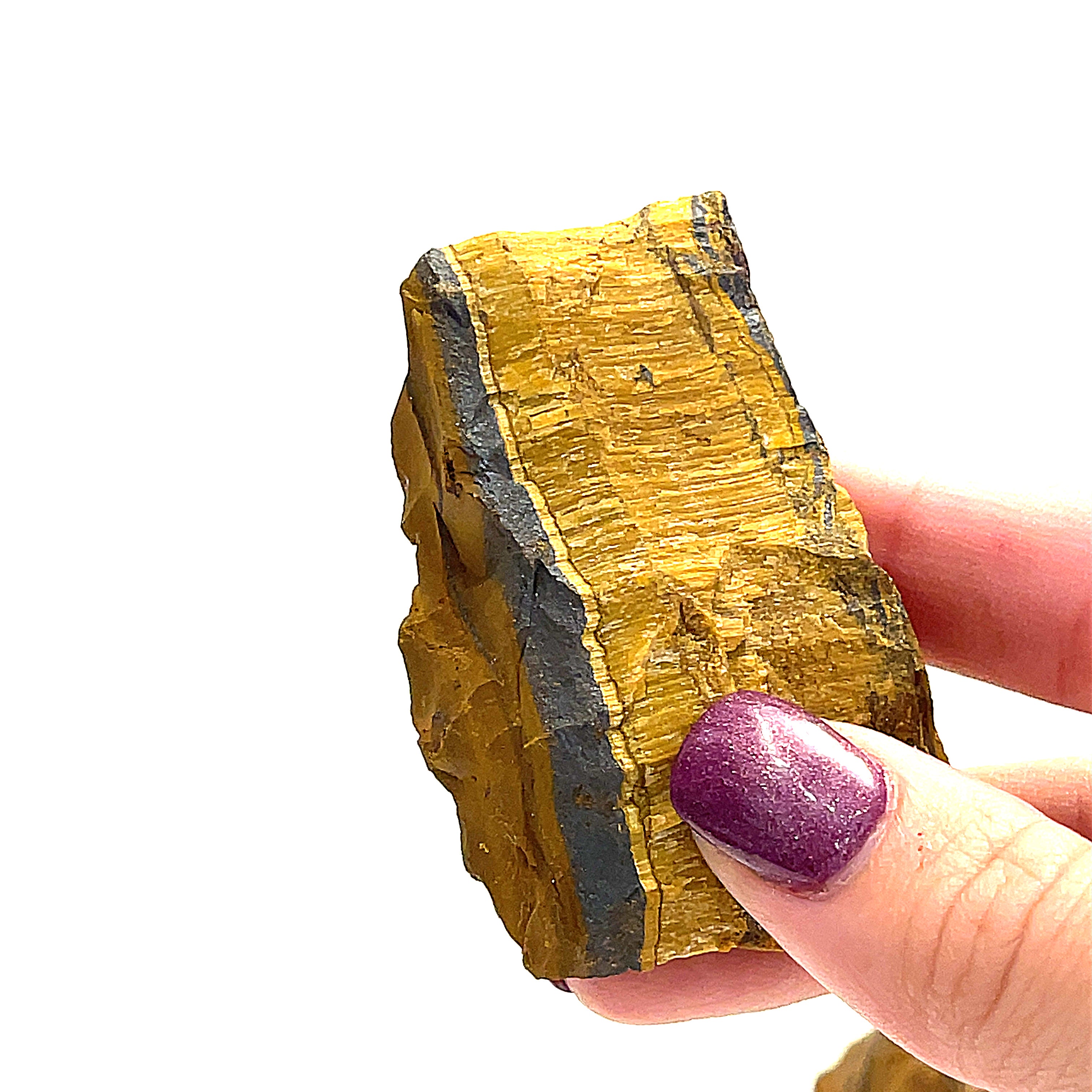 A large pieces of raw golden tiger eye gemstones is displayed in a models finger tips, on a white background, in a front overview. 
