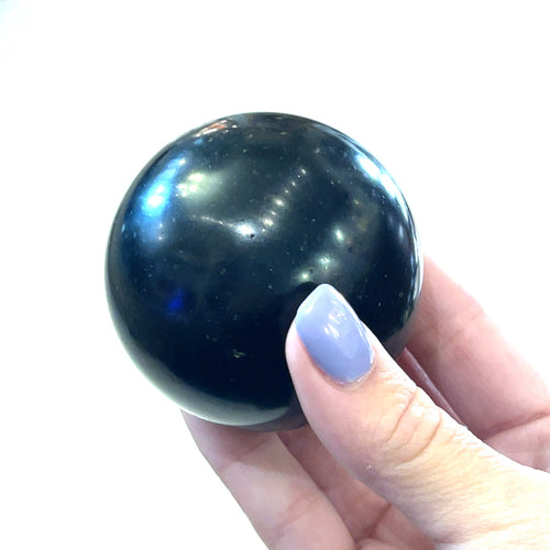 A model holding a Black Tourmaline Sphere used for energy grounding and meditation on a white background front view. 