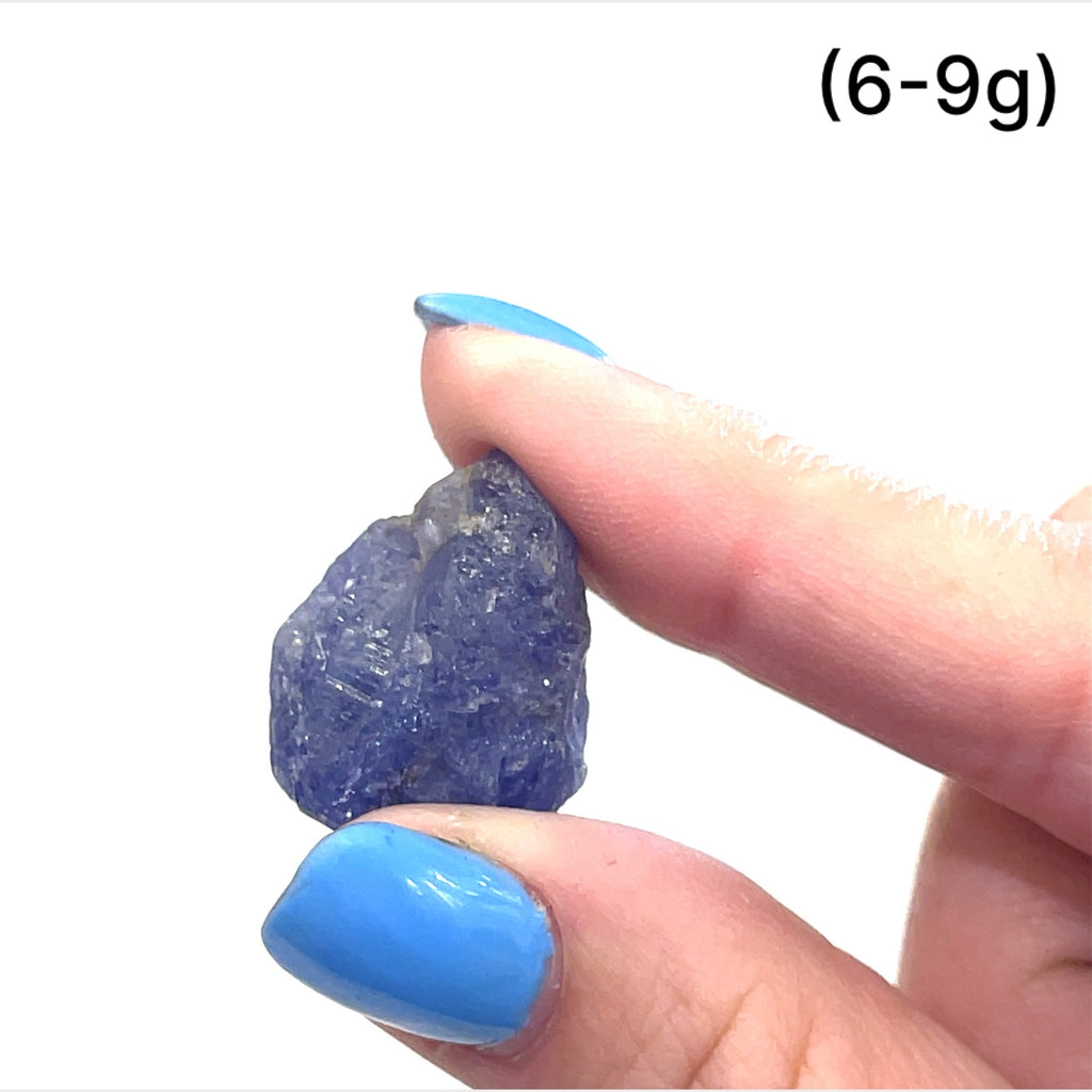 A model's hand holding a raw Tanzanite gemstone, with a focus on its deep blue color, on a white background, front view. size (6-9g)