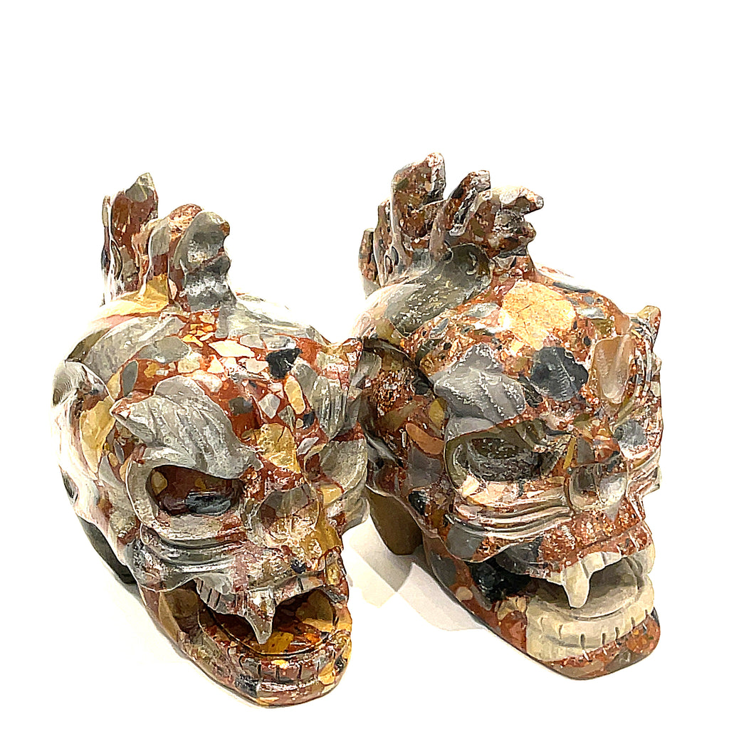 A pair of carved jasper skull alter stones with a dragon mohawk design on a white background, slightly right-angle front view. 