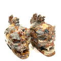 A pair of carved jasper skull alter stones with a dragon mohawk design on a white background, slightly right-angle front view. 