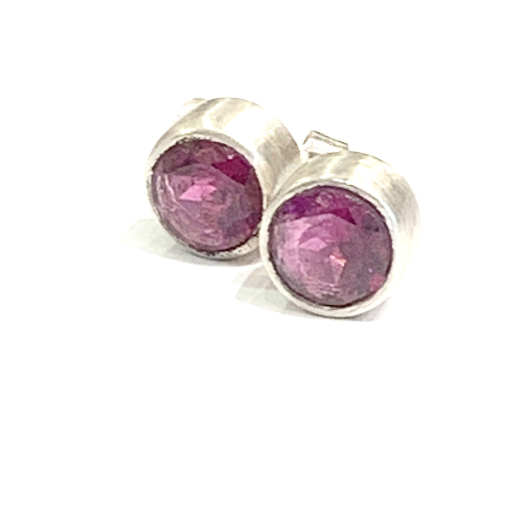 A pair of faceted ruby gemstone round tube-set earrings with sterling silver tube settings on a white background, front overview.