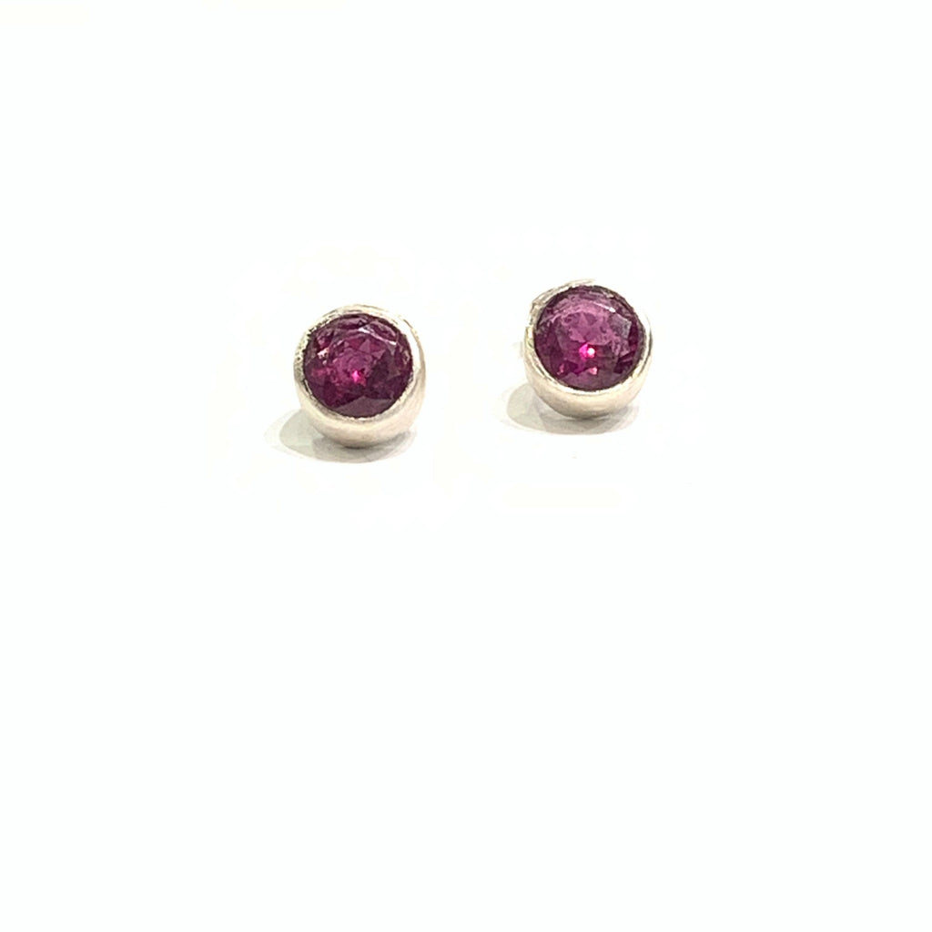 A pair of faceted ruby gemstone round tube-set earrings with sterling silver tube settings on a white background, top center overview.