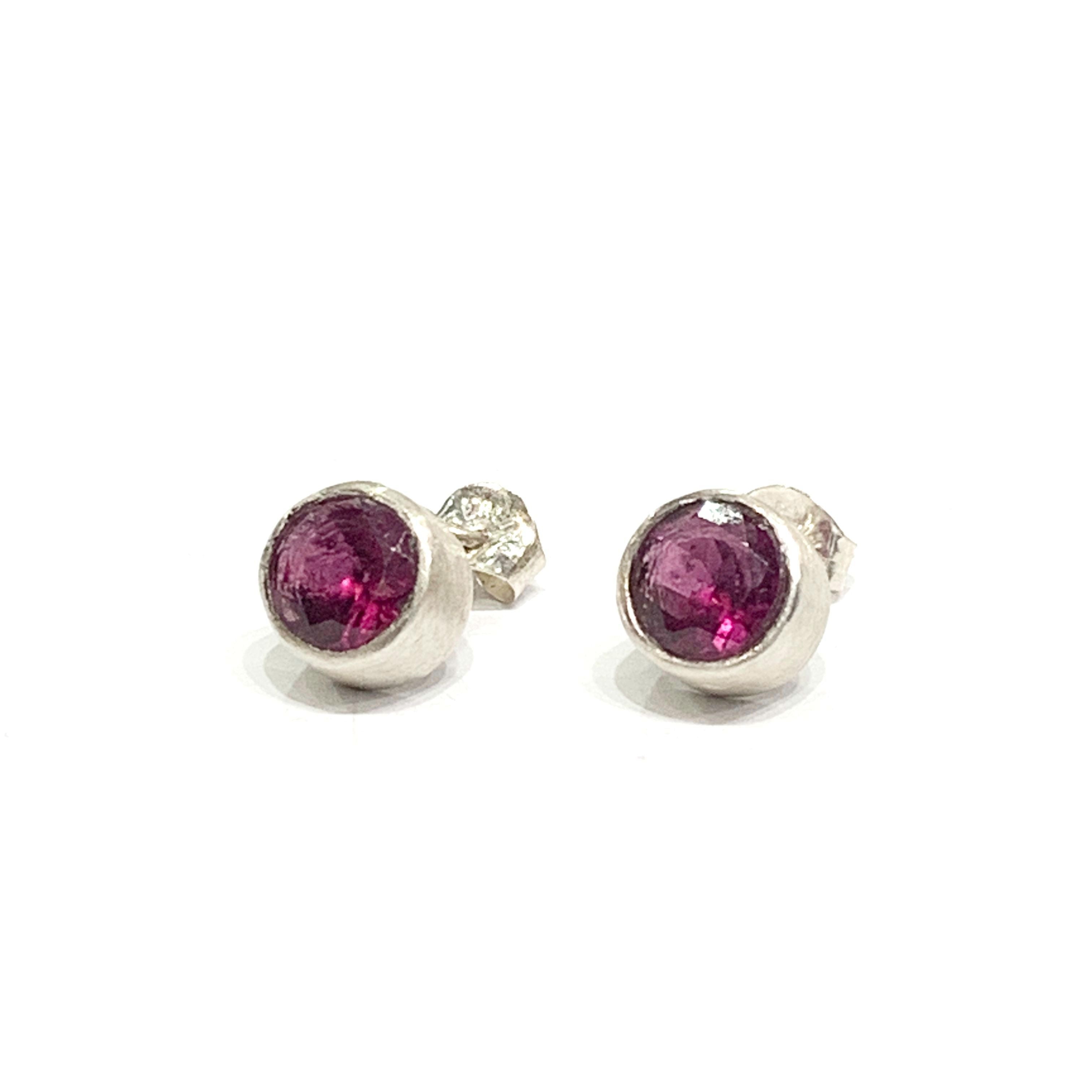 A pair of faceted ruby gemstone round tube-set earrings with sterling silver tube settings on a white background, top overview.