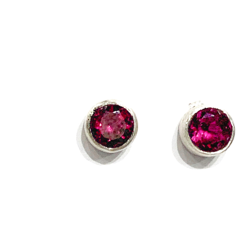 A pair of faceted ruby gemstone round tube-set earrings with sterling silver tube settings on a white background, top view.
