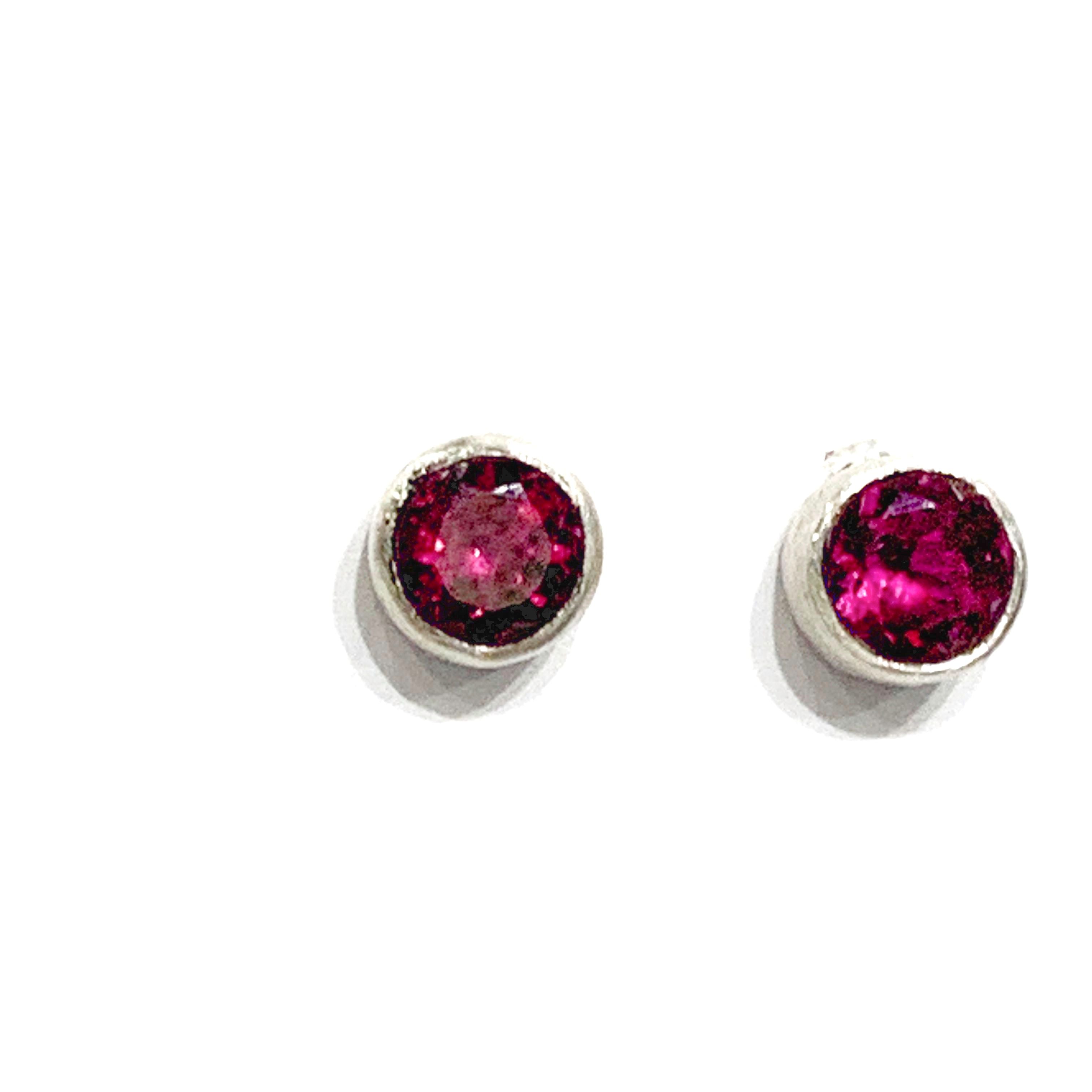 A pair of faceted ruby gemstone round tube-set earrings with sterling silver tube settings on a white background, top view.