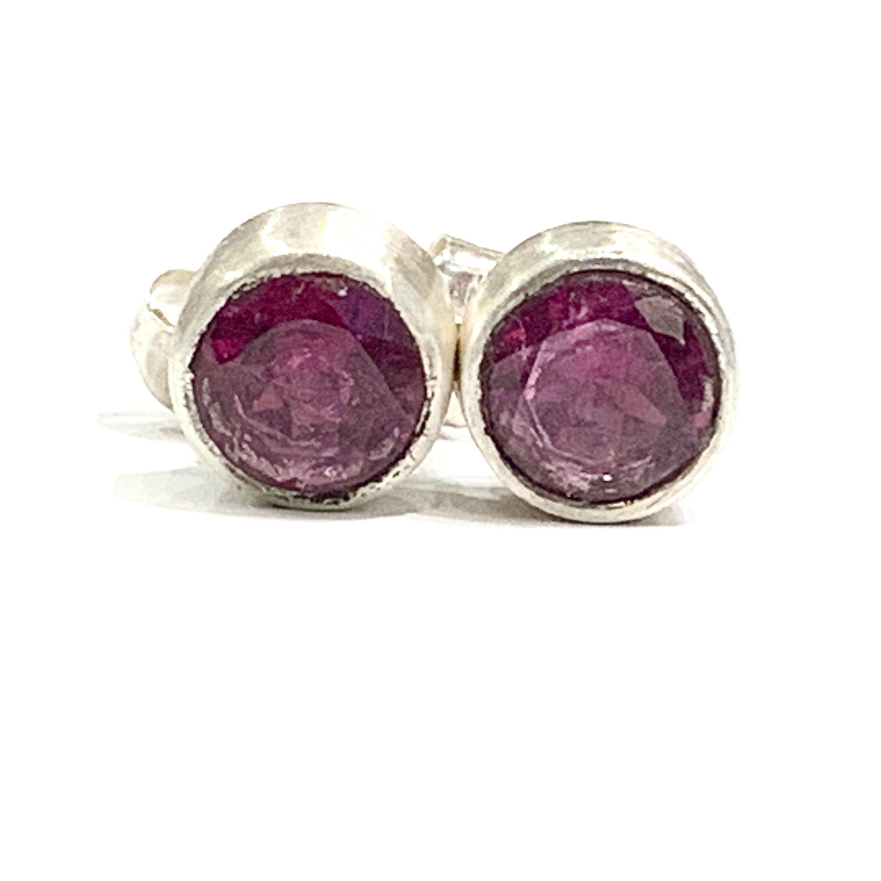 A pair of faceted ruby gemstone round tube-set earrings with sterling silver wire basket settings on a white background, front close up view.