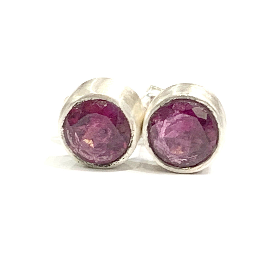 A pair of faceted ruby gemstone round tube-set earrings with sterling silver wire basket settings on a white background, front view.