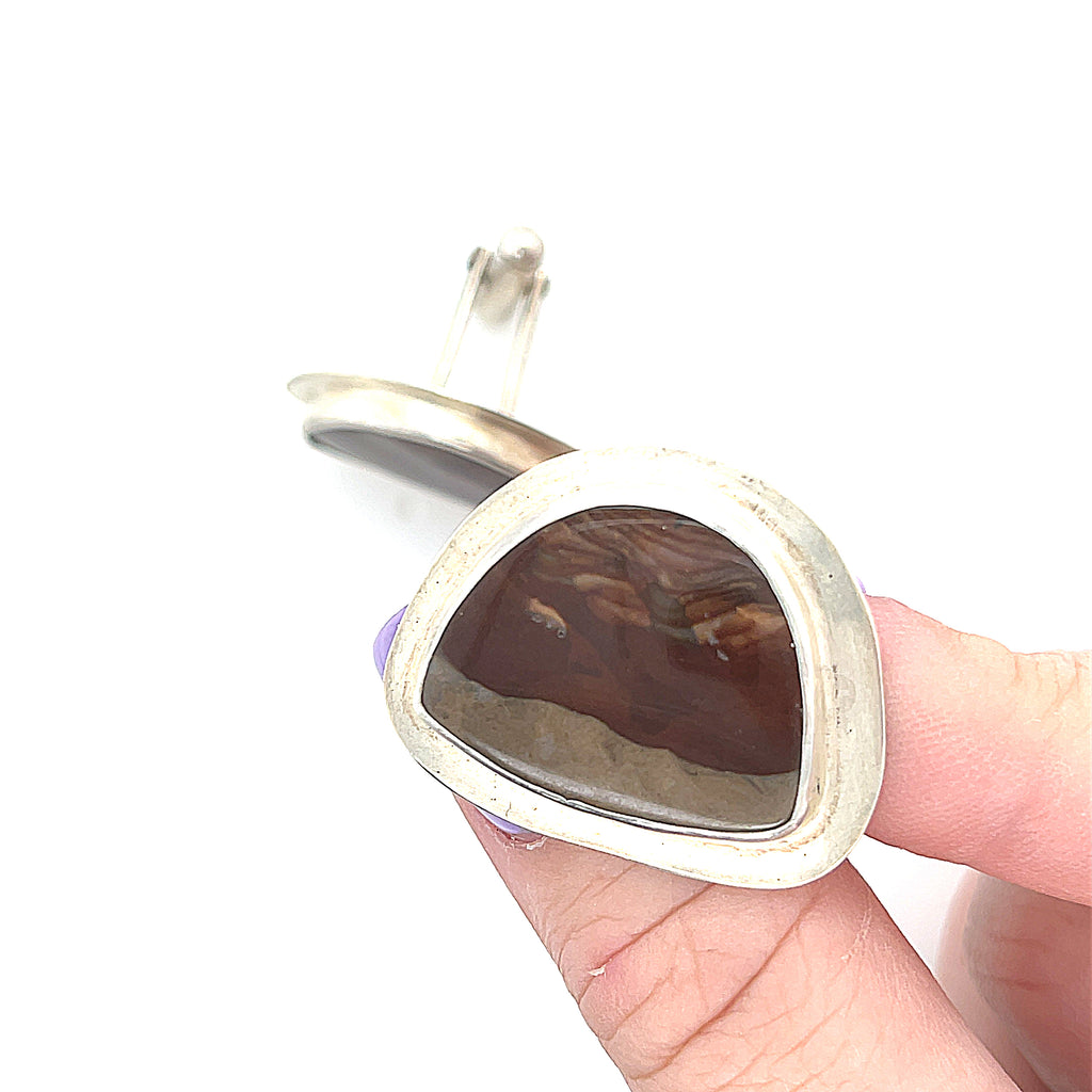 A pair of sterling silver cufflinks featuring rounded-triangle-shaped mookite jasper gemstones, bezel-set in a round sterling silver setting. On a white background, front close up view in a models fingertips.