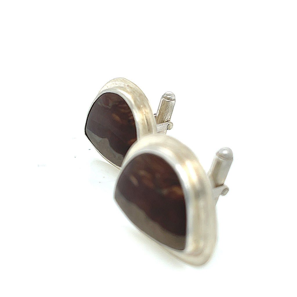 A pair of sterling silver cufflinks featuring rounded-triangle-shaped mookite jasper gemstones, bezel-set in a round sterling silver setting. On a white background, left-angle front view.