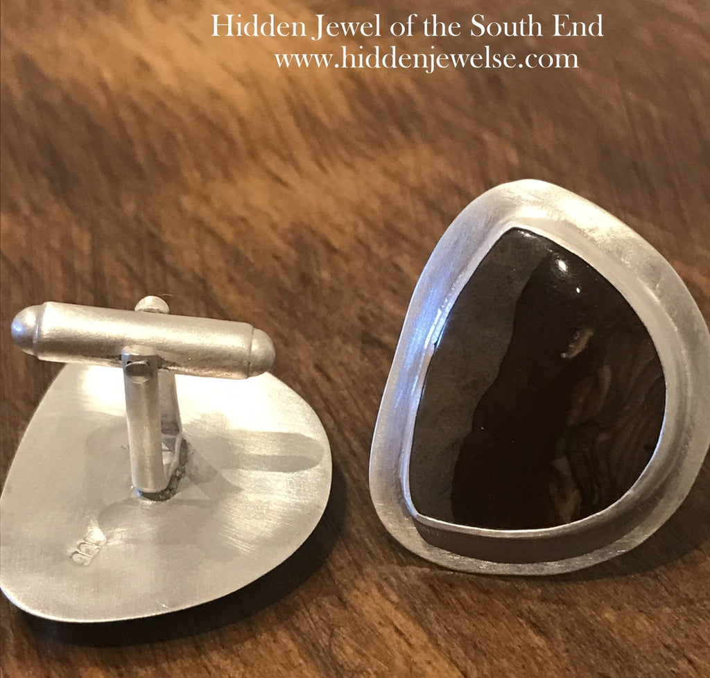 A pair of sterling silver cufflinks featuring rounded-triangle-shaped mookite jasper gemstones, bezel-set in a round sterling silver setting. On a wood background, close up one front and one back view.