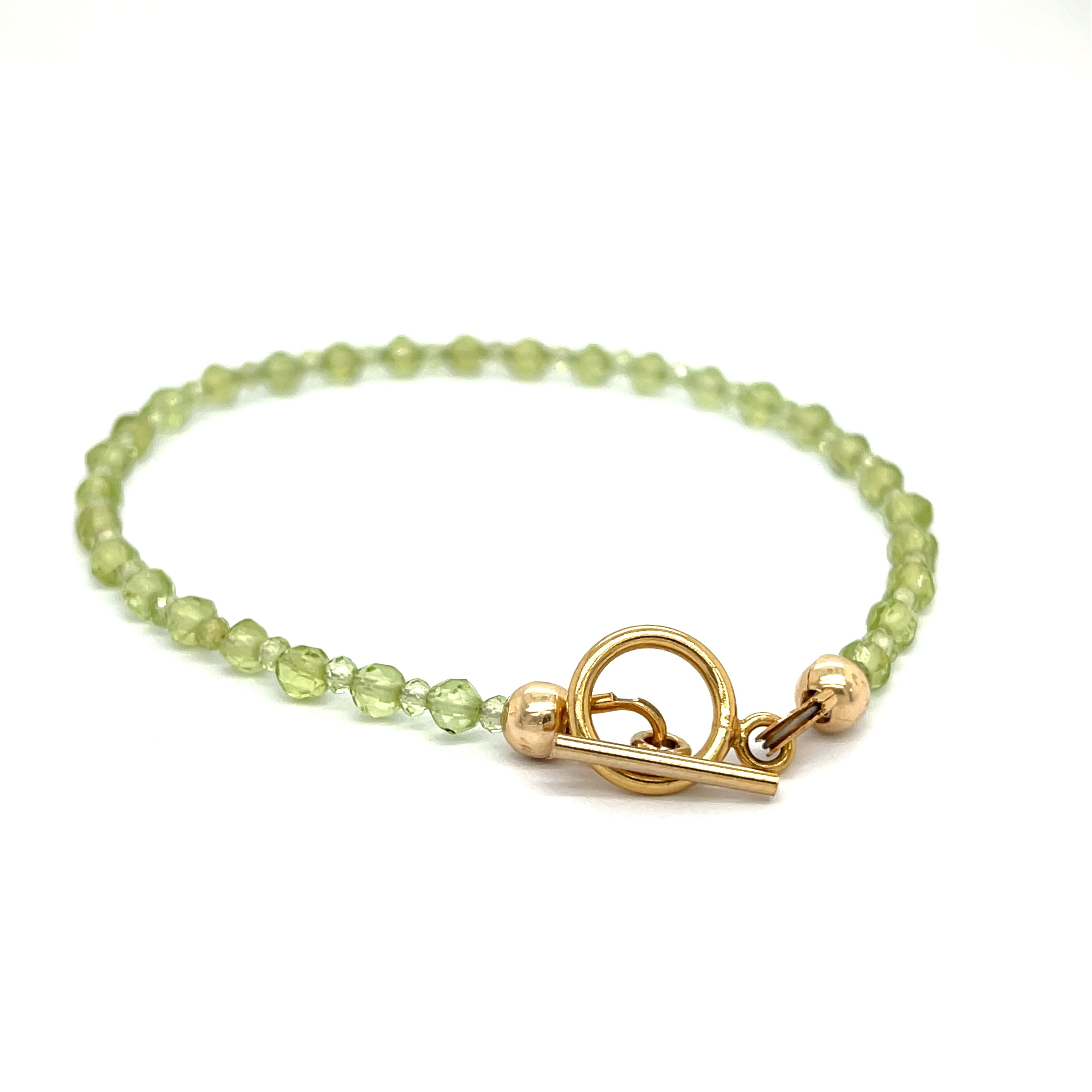 A peridot gemstone 2-3mm faceted round with a gold filled toggle on a white background back center overview.