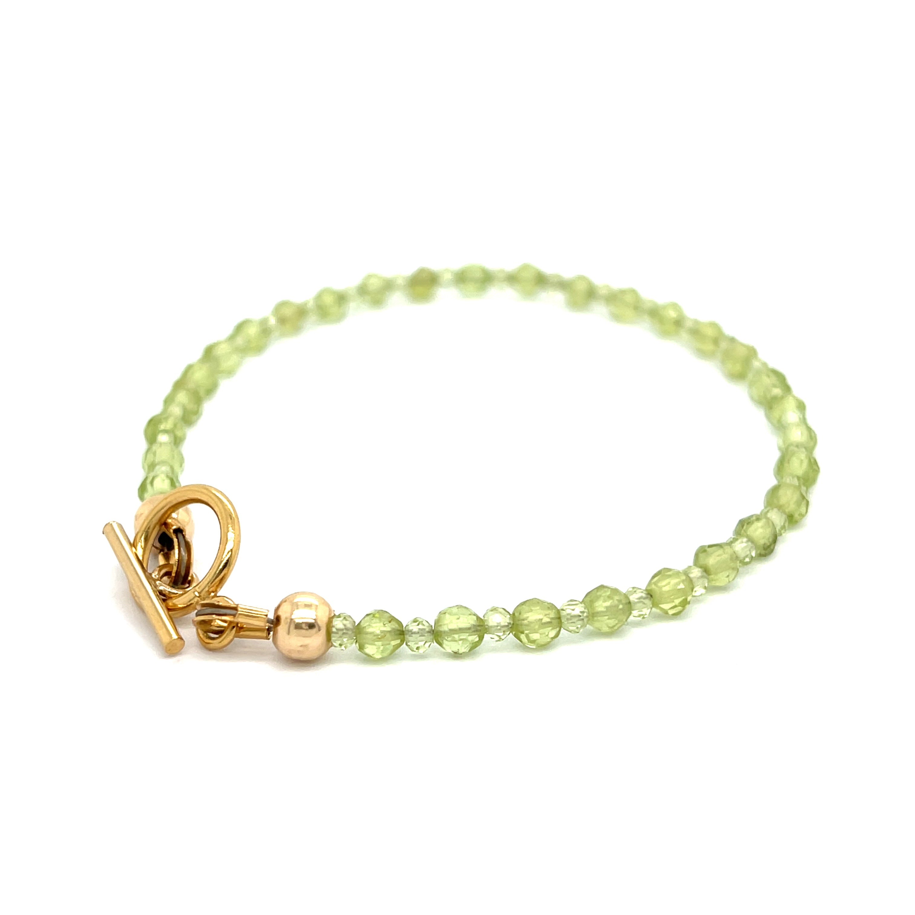 A peridot gemstone 2-3mm faceted round with a gold filled toggle on a white background back left angle overview.